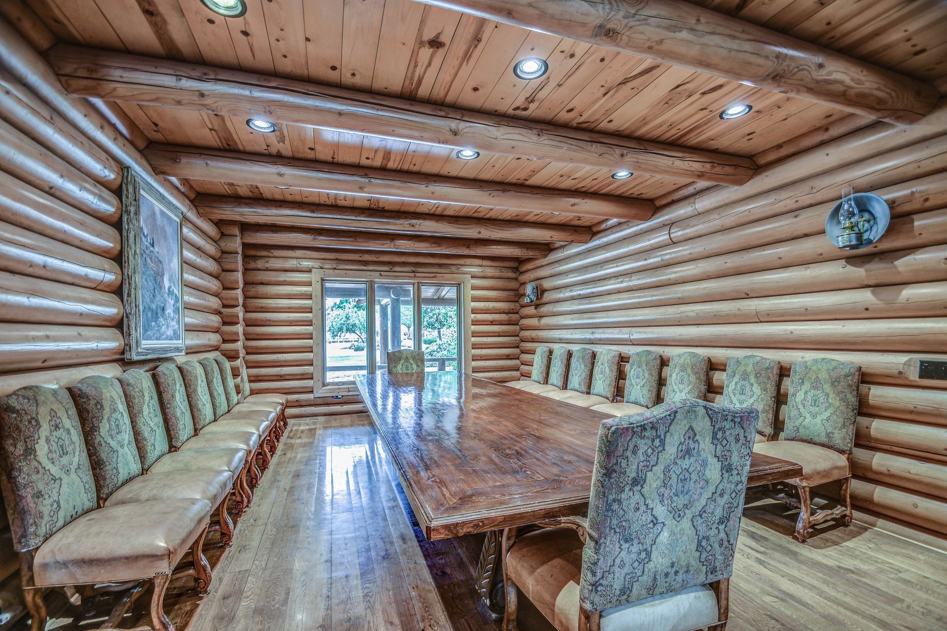 Wood-paneled log cabin dining room with long table, upholstered benches, and glass doors at the far end