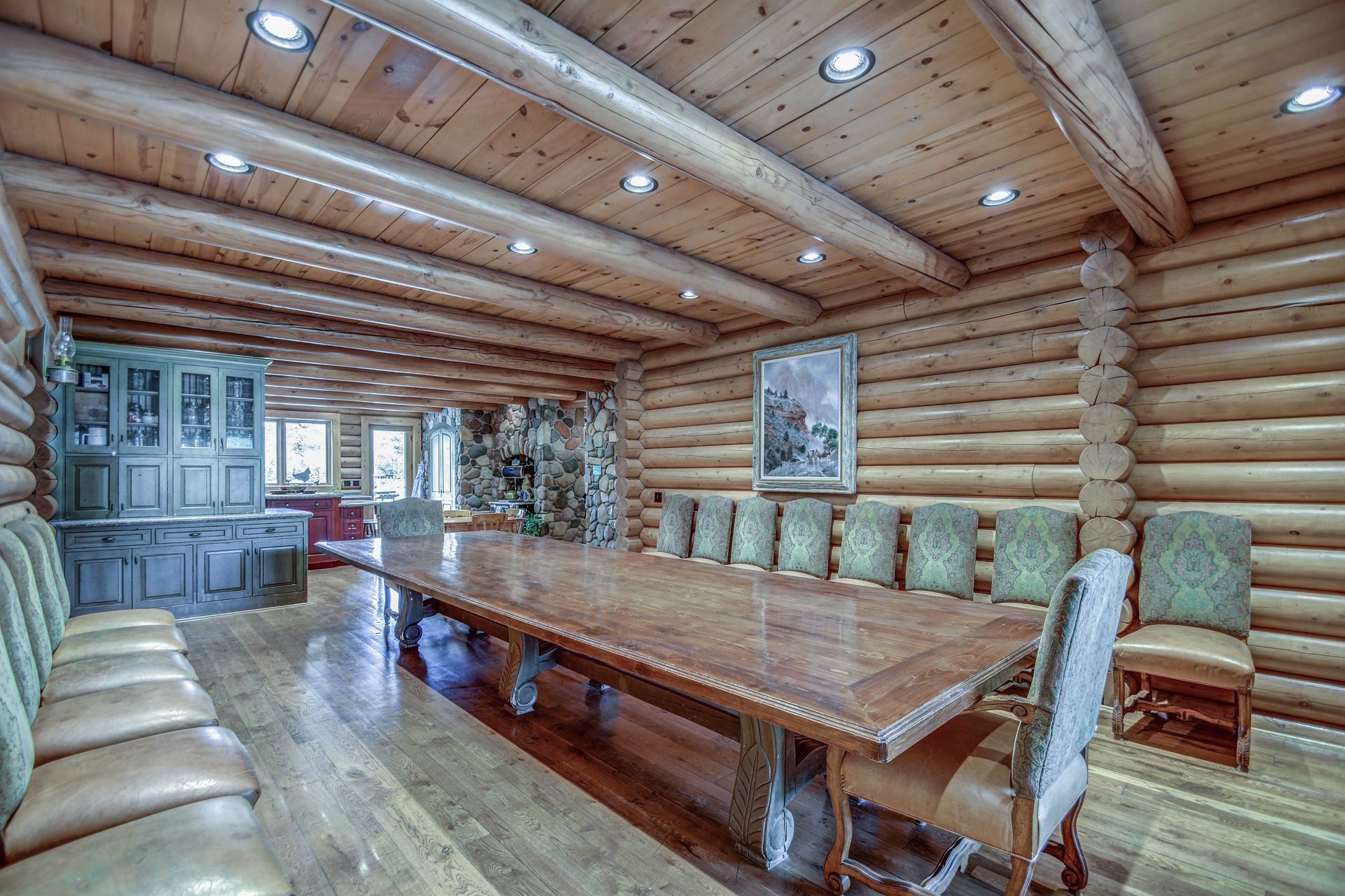 Rustic log dining room with a long wooden table, upholstered chairs, and a cabinet