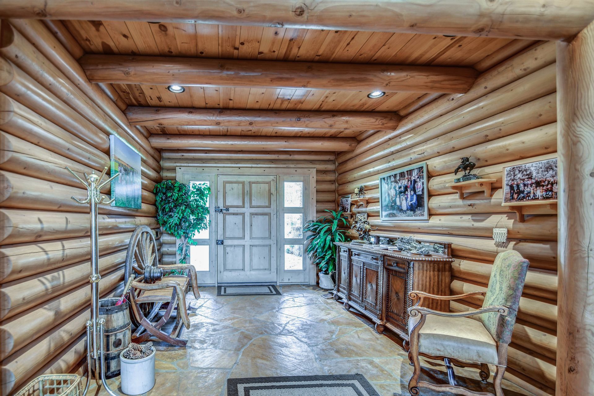 Log cabin hallway with wooden walls, stone floor, furniture, and framed artwork leading to a white door