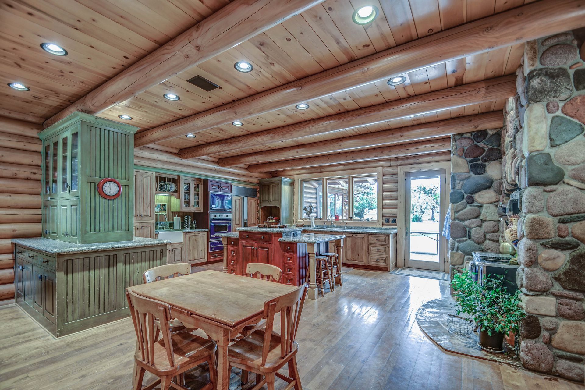 Rustic log cabin dining area with wooden tables, stone fireplace, and large windows overlooking the outdoors