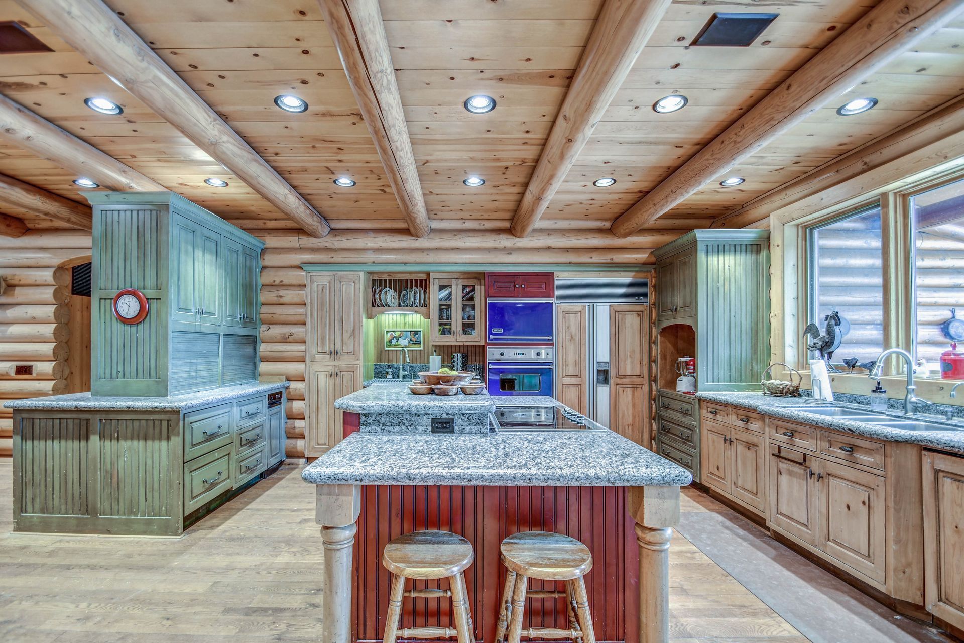 Wood-paneled kitchen with granite island, stools, and blue cabinets beneath a wood ceiling