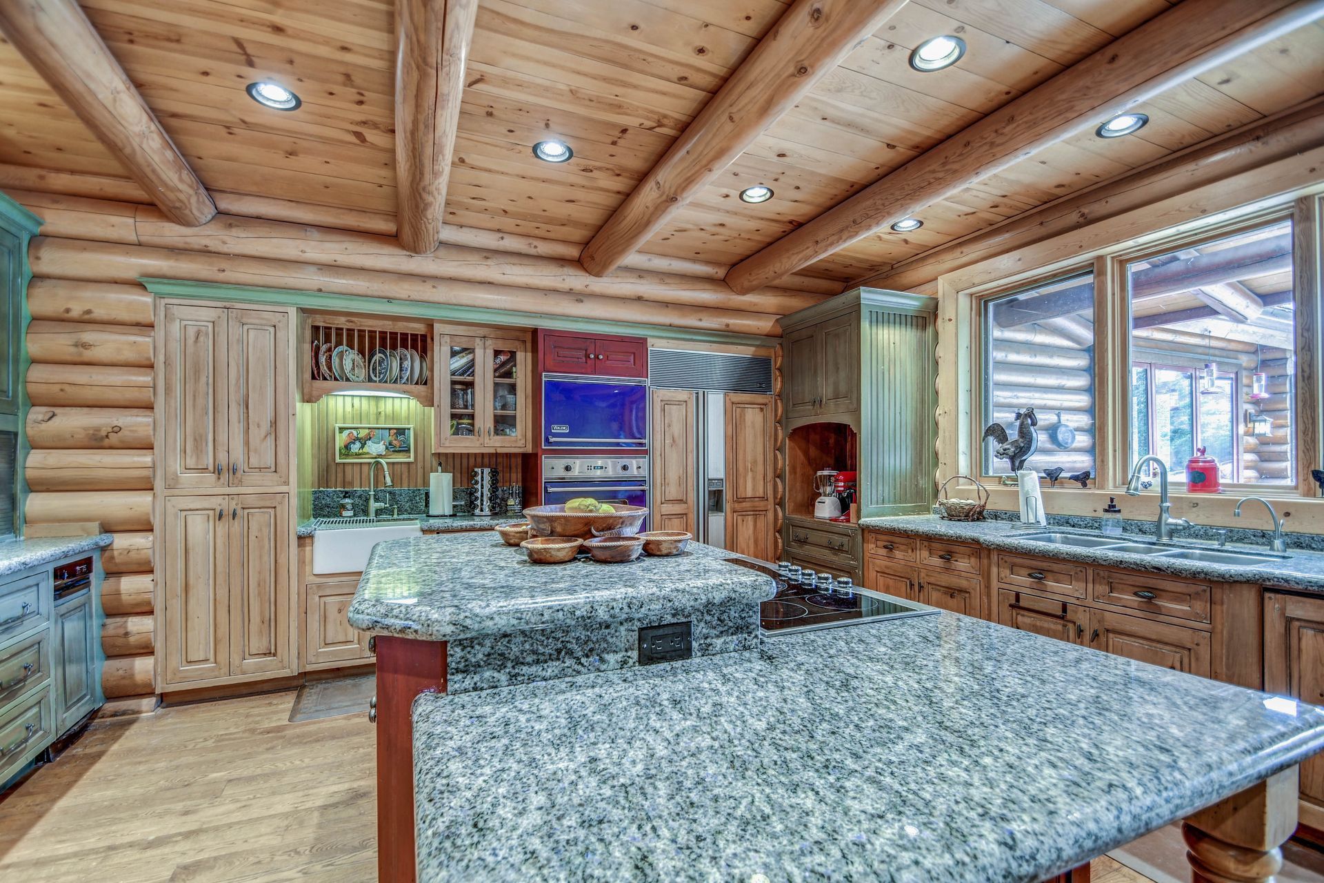 Rustic kitchen with wood-paneled ceiling, granite island, and large windows looking out to snowy trees