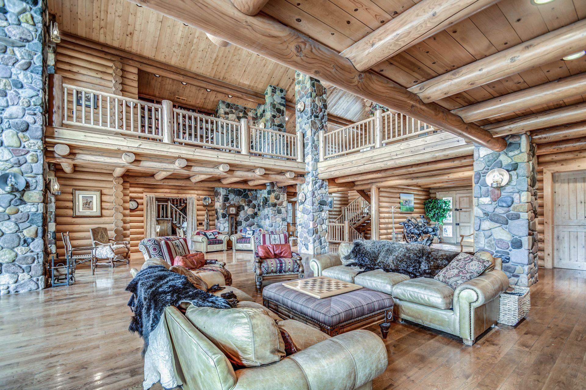 Rustic log cabin living room with stone fireplace, loft balcony, and leather sofas