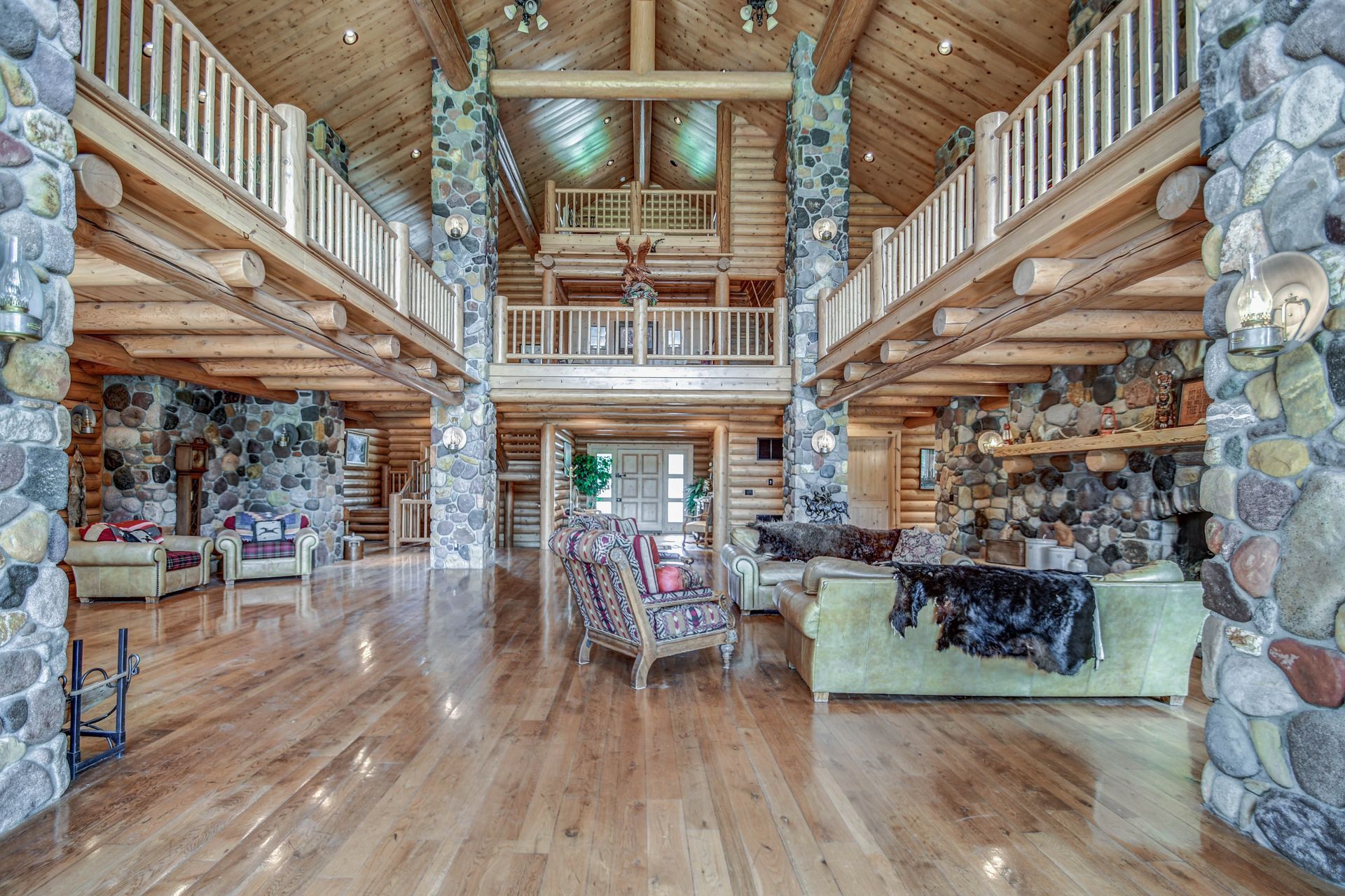 Spacious rustic lodge interior with stone columns, wood beams, balcony railing, and polished wooden floors