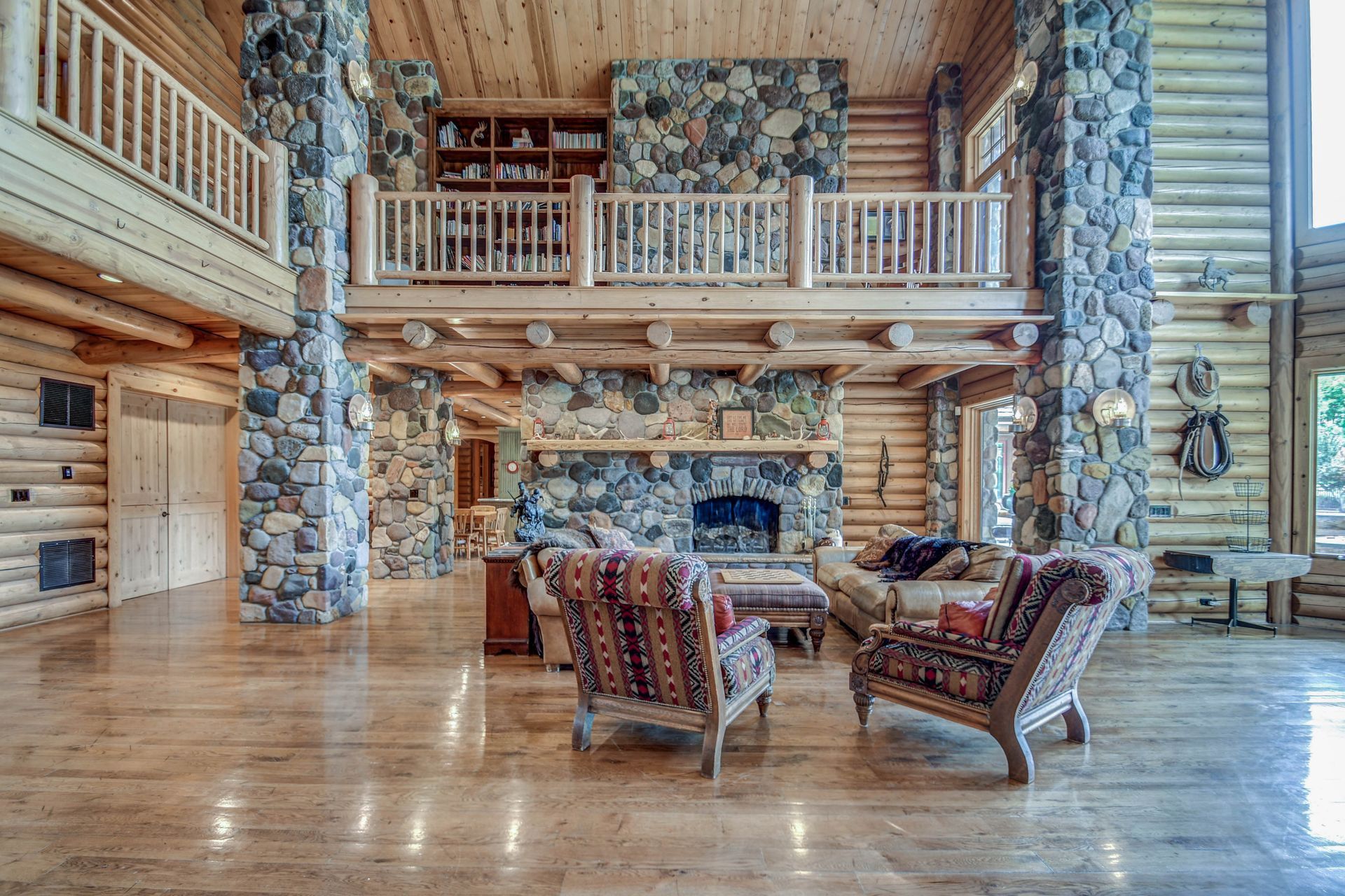 Rustic lodge lobby with stone fireplace, wood beams, loft balcony, and leather chairs around a seating area