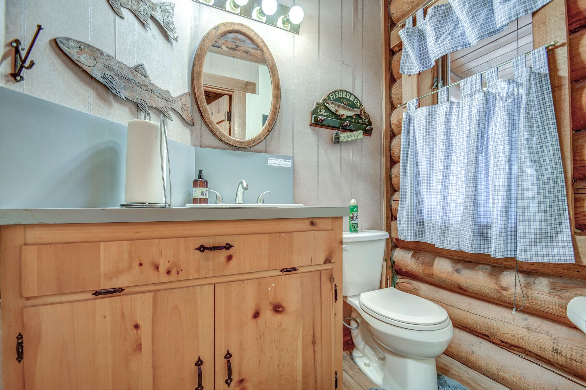 Rustic bathroom with wood vanity, round mirror, white toilet, and blue curtain by a log wall