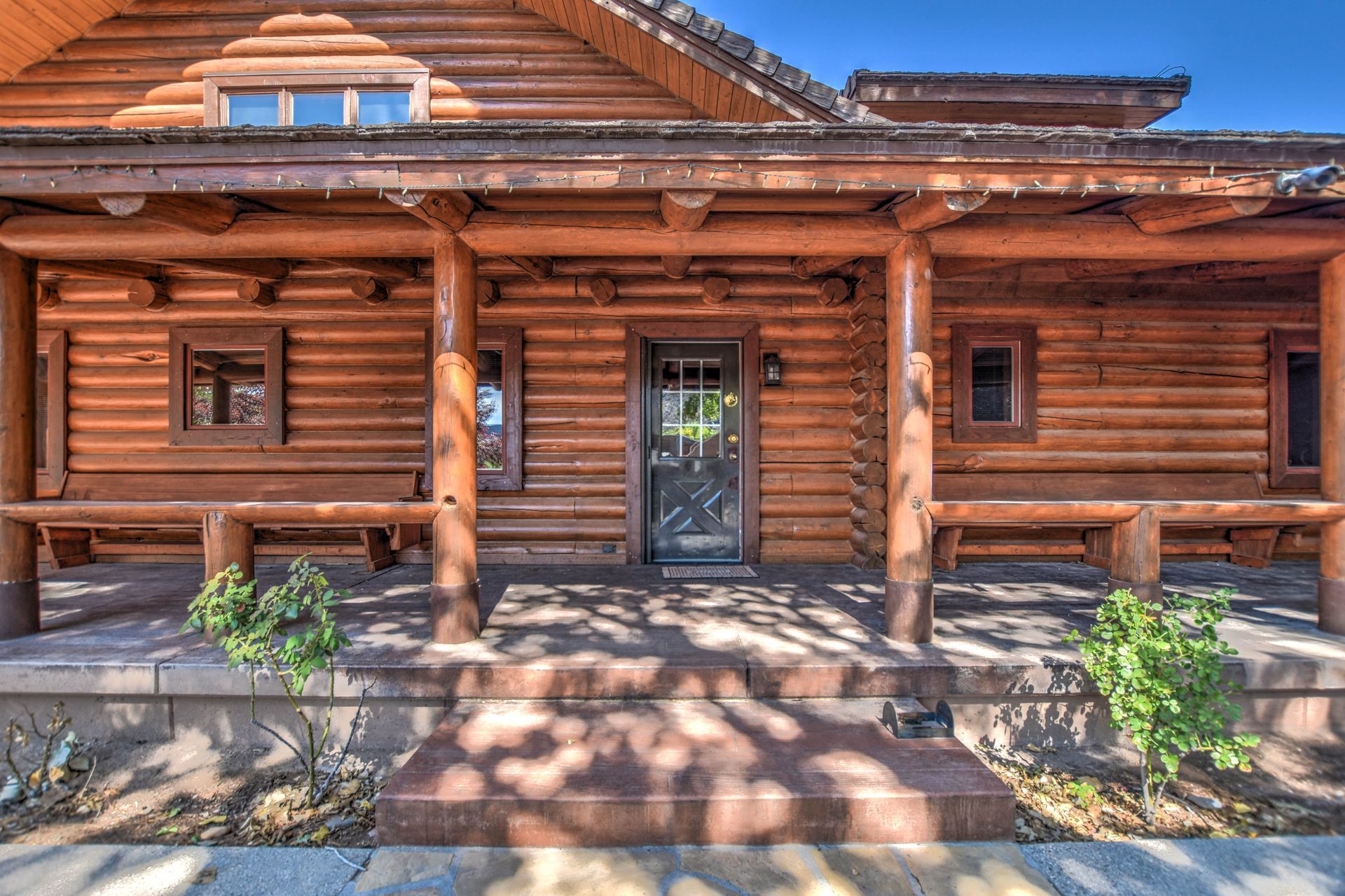 Rustic log cabin porch with wooden columns, central door, and sunlight casting shadows on stone steps