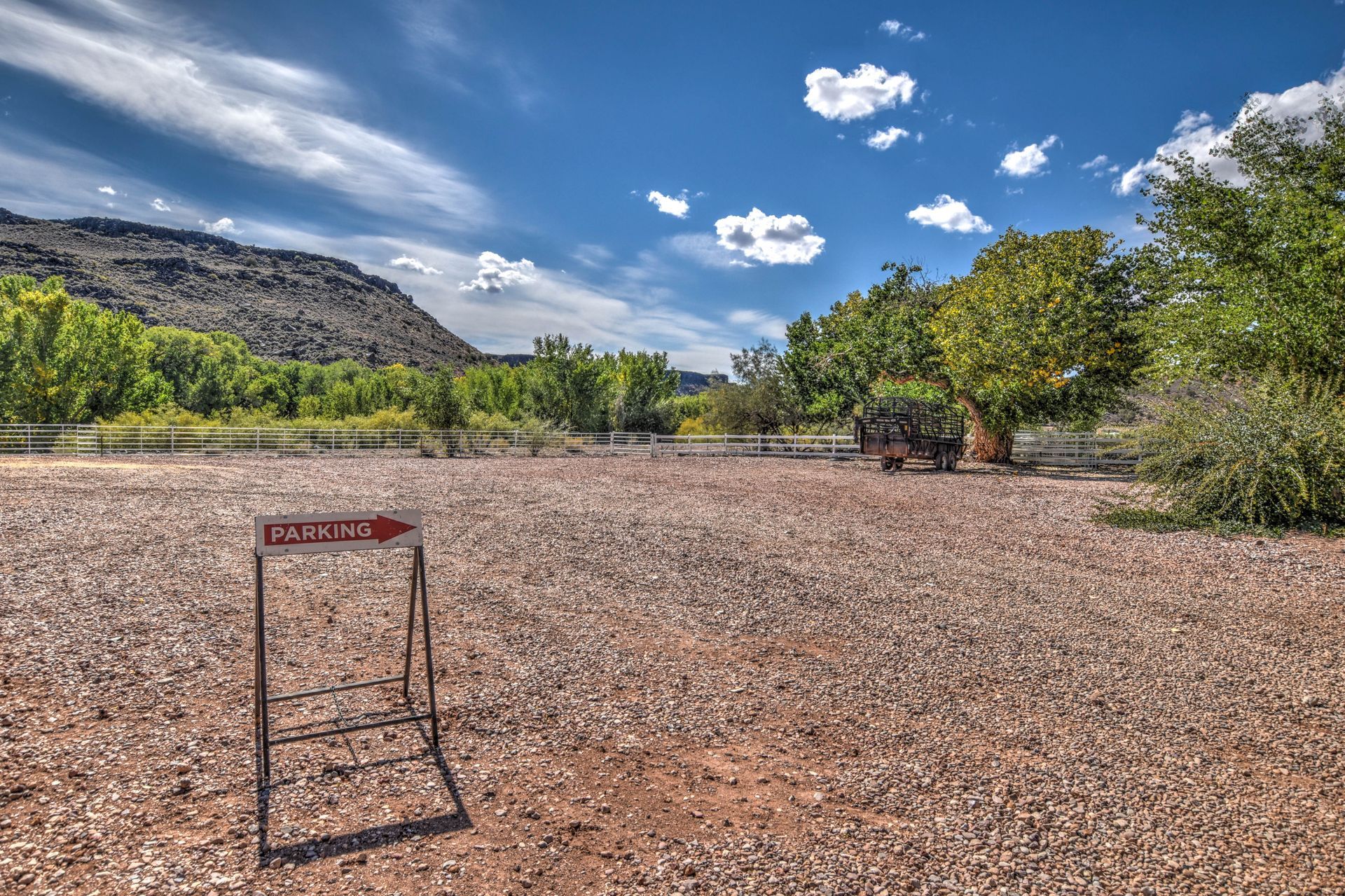 Desert trailhead sign in a rocky landscape with trees and mountains under a blue sky with clouds