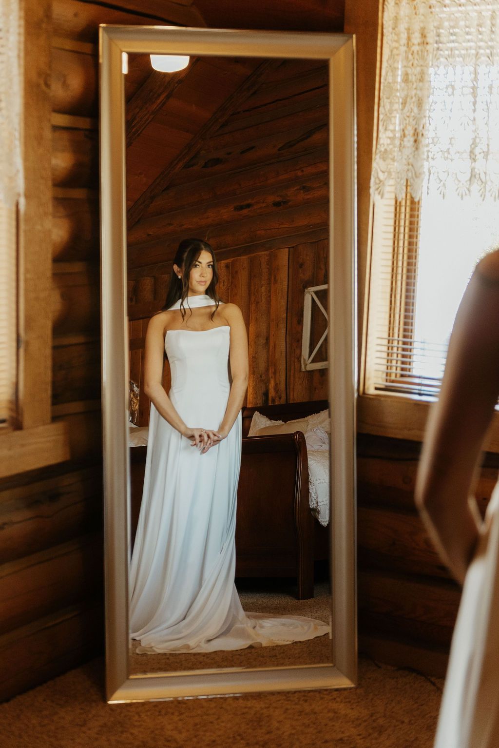 Woman in a white dress standing in a mirror inside a rustic wooden room