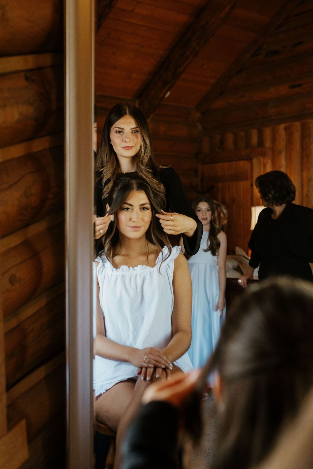 Women seated in a wooden room, one in white centered in the foreground, others standing behind