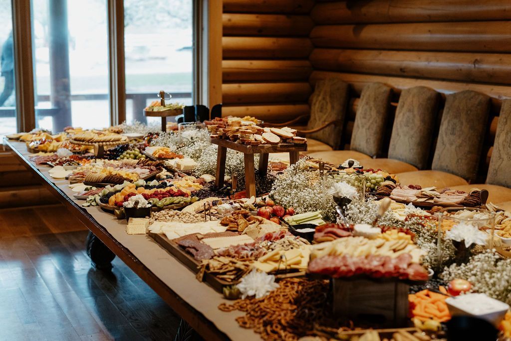 Long buffet table in a rustic log-cabin dining room, filled with assorted appetizers and desserts.