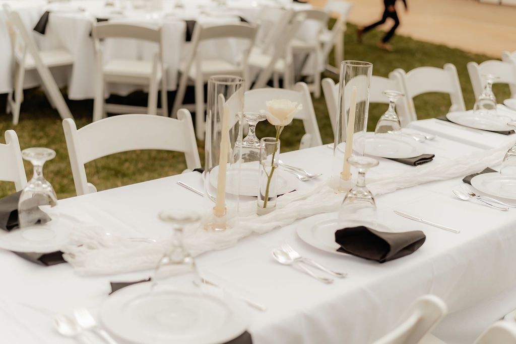 White banquet tables and chairs set with plates, glasses, and napkins for an outdoor event