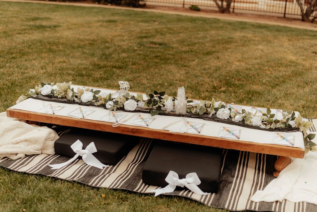 White floral wreath on a wooden bench with striped blankets in a grassy outdoor setting