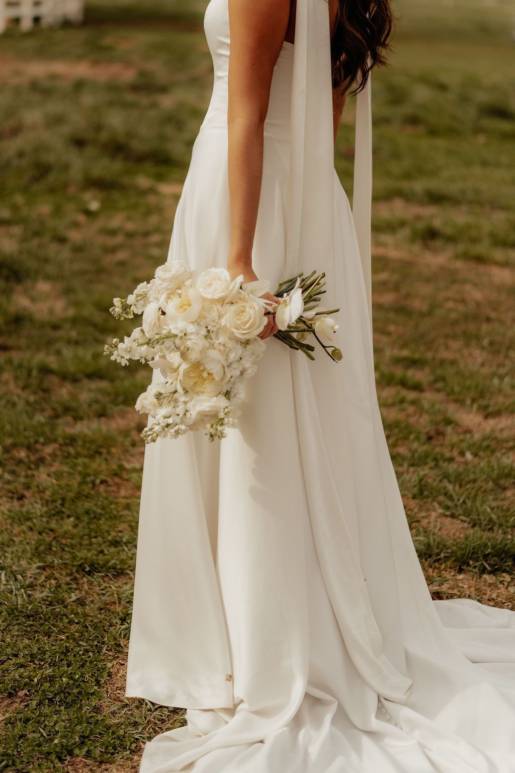 Bride holding a white bouquet beside a flowing ivory wedding dress outdoors