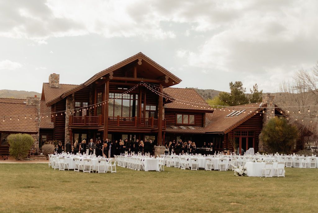 Outdoor wedding ceremony at a rustic lodge with white chairs and guests gathered on the lawn
