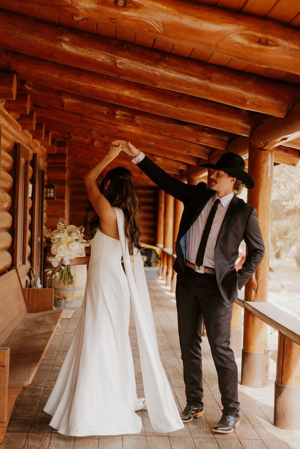 Bride and groom dancing under a wooden porch, with the bride in a white gown and the groom in a black hat.