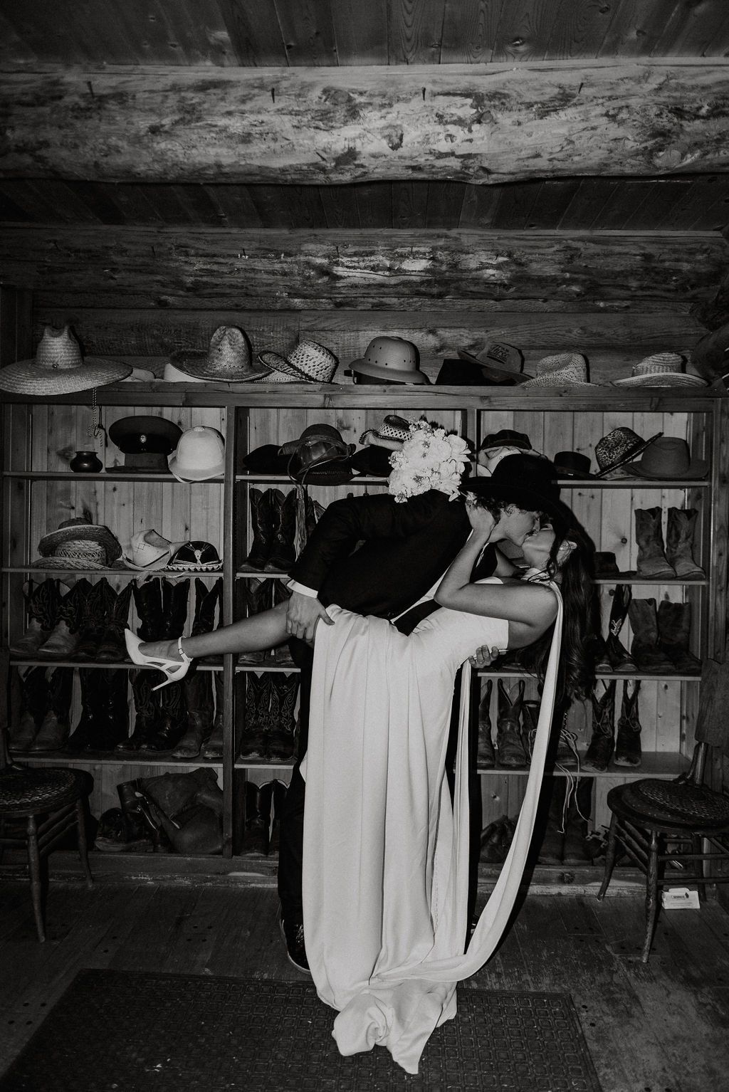 Two performers in flowing costumes pose in a studio with shelves and hats in the background