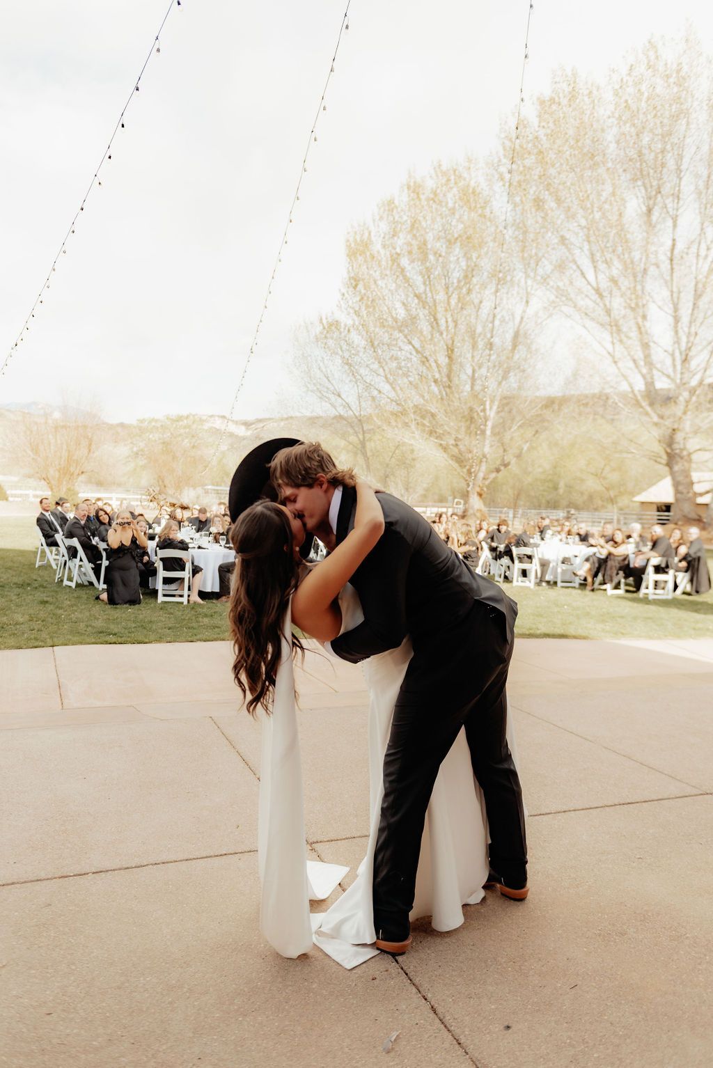 Couple embracing and kissing under a white wedding canopy during an outdoor reception