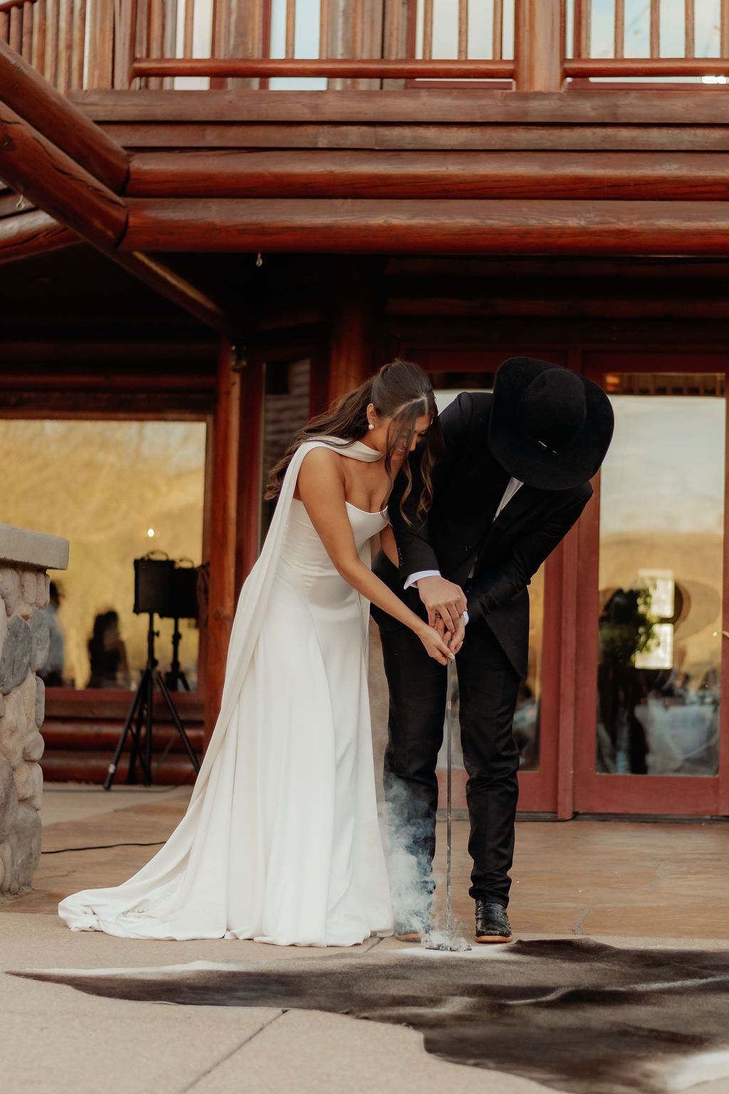 Bride and groom leaning together outside a rustic building, holding hands and looking down.