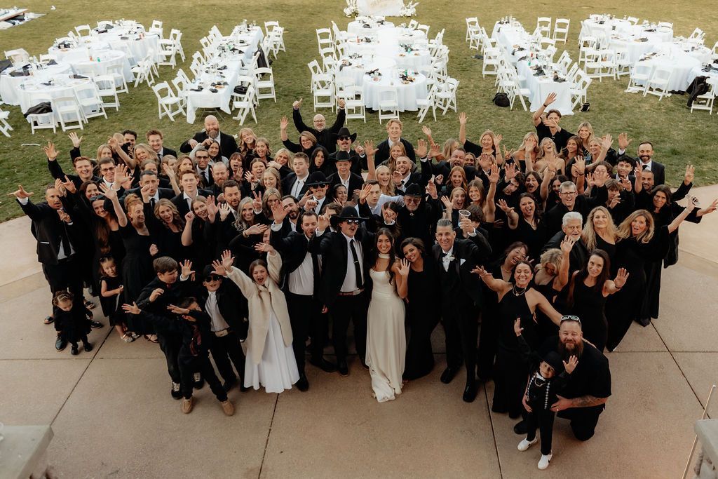 Large group posing outdoors on a walkway near rows of white chairs, many waving at the camera