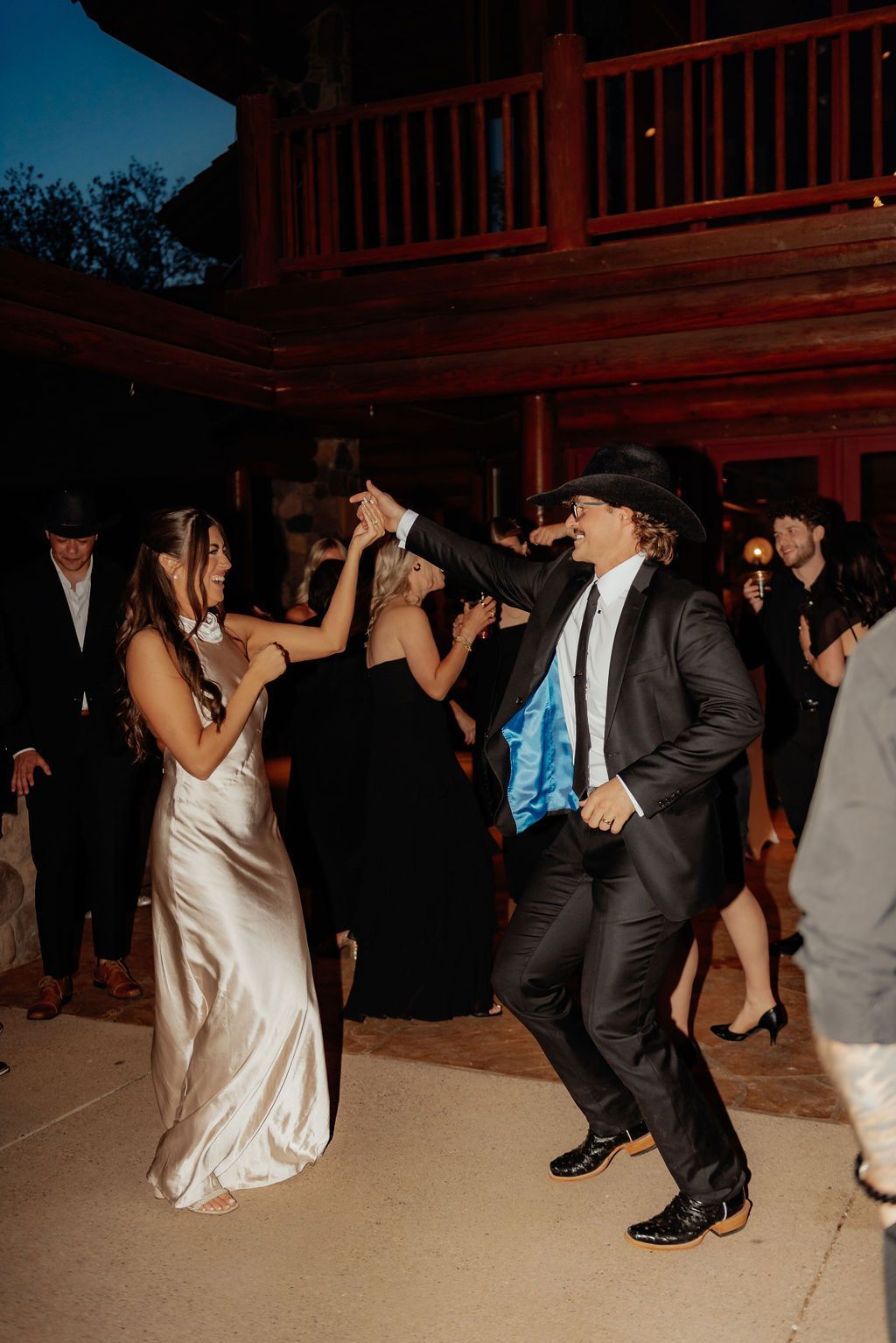 People dancing at an outdoor evening event, with a man in a black suit and blue tie at center.