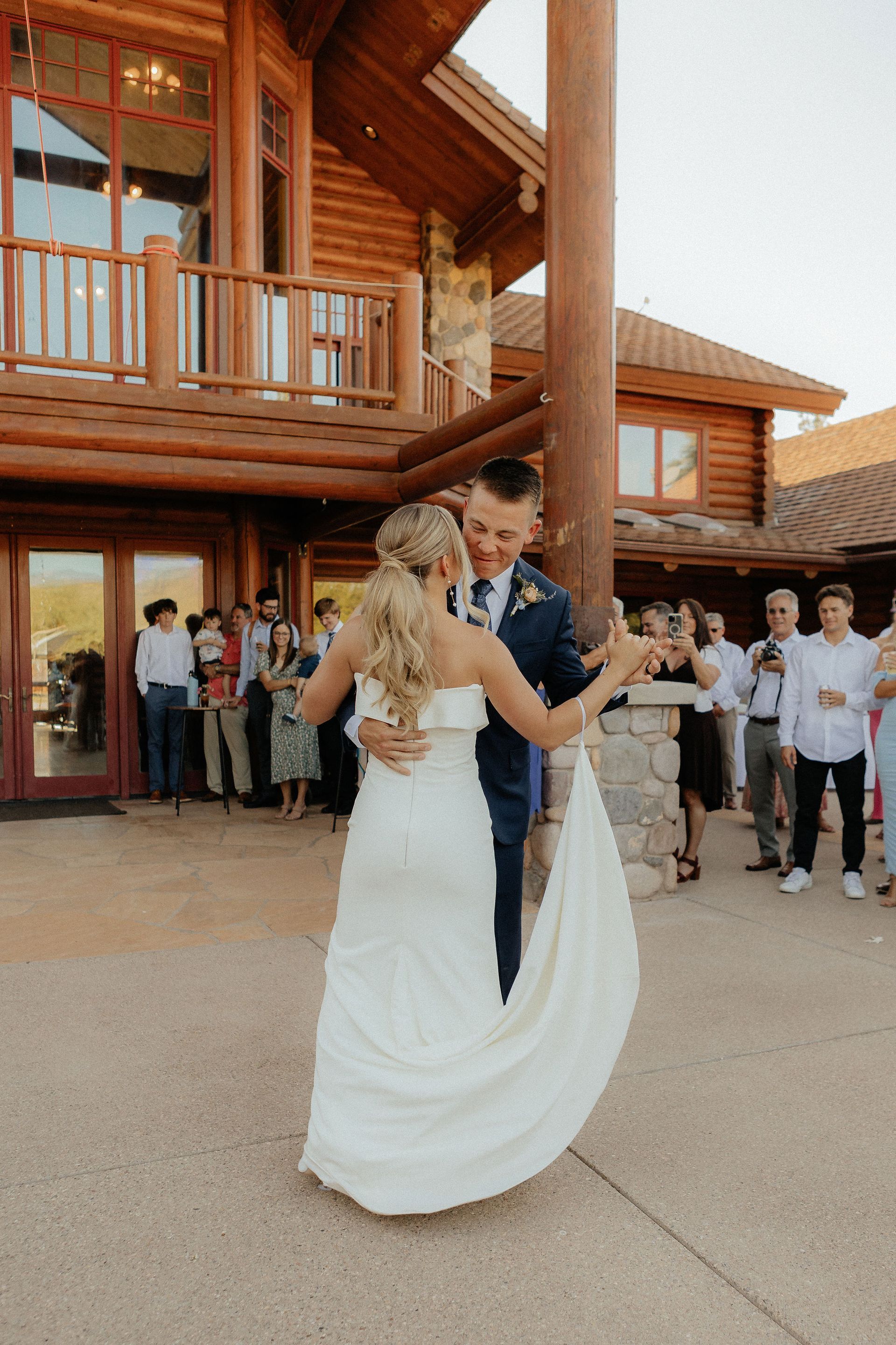 Bride and groom dancing outside a wooden lodge while guests watch nearby