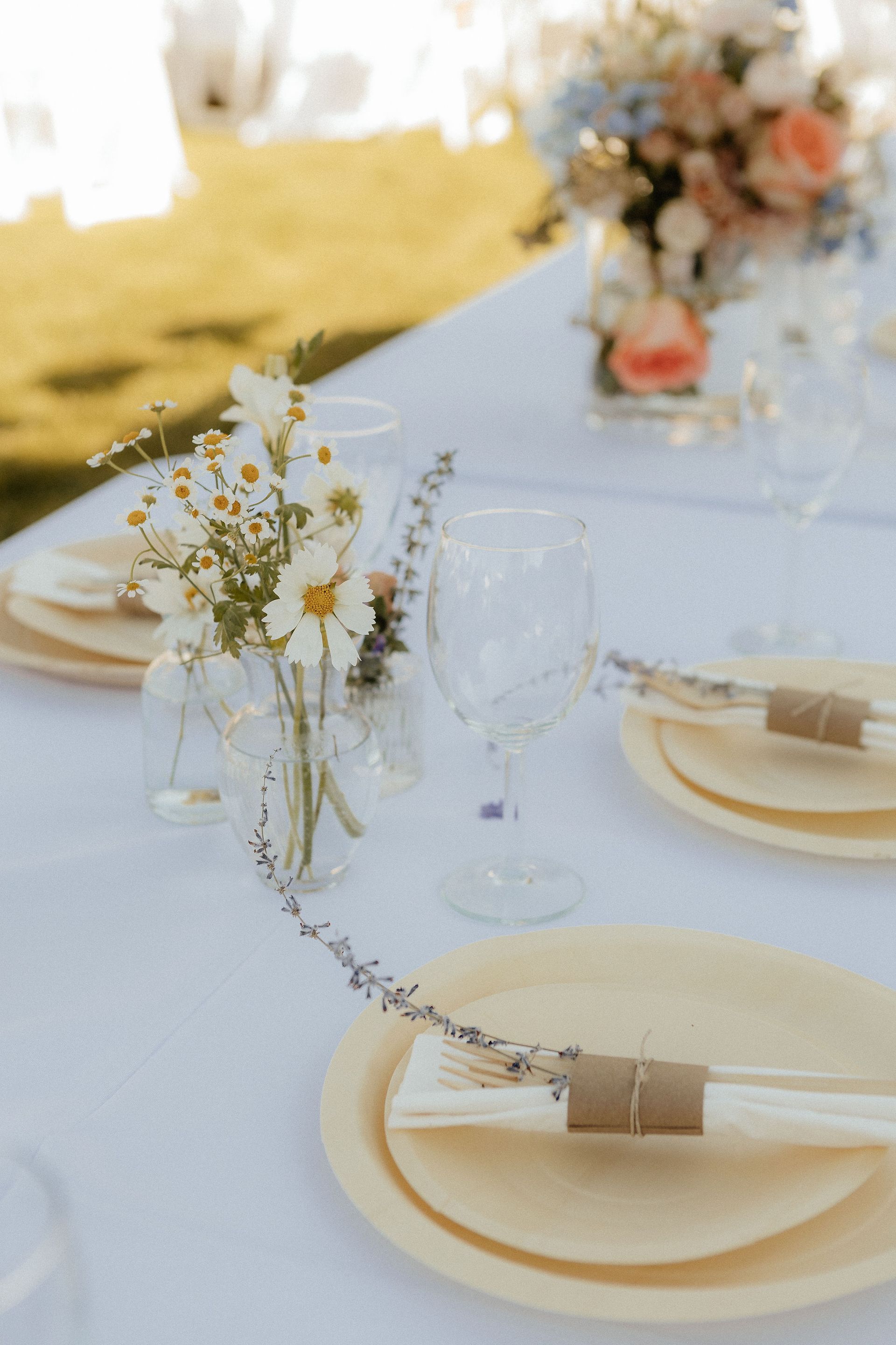 Elegant outdoor table setting with white plates, gold accents, and floral centerpieces on a white tablecloth
