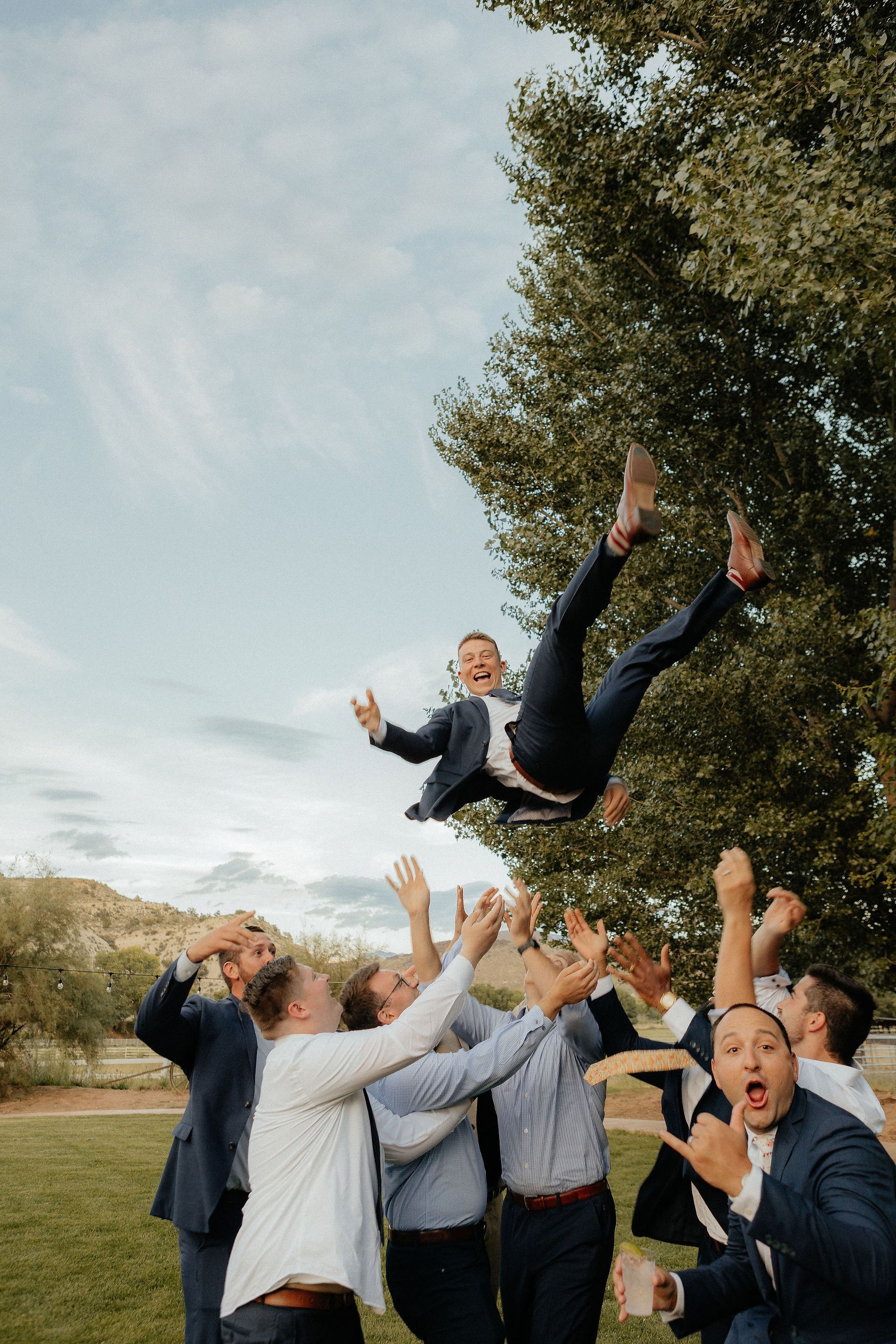 Group outdoors tossing a smiling person into the air beneath a tree