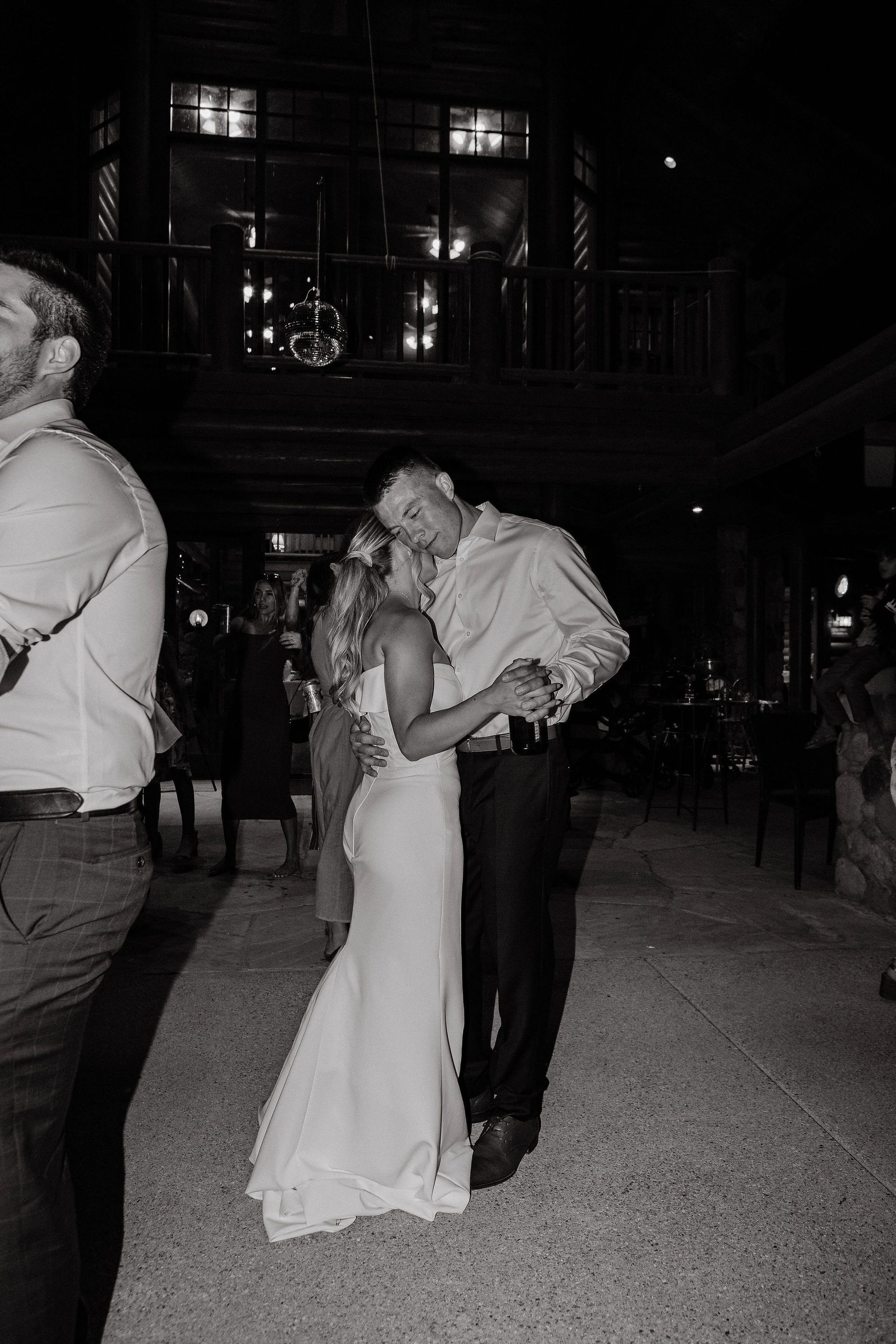 A couple in formal attire kissing in a dimly lit outdoor venue at night.