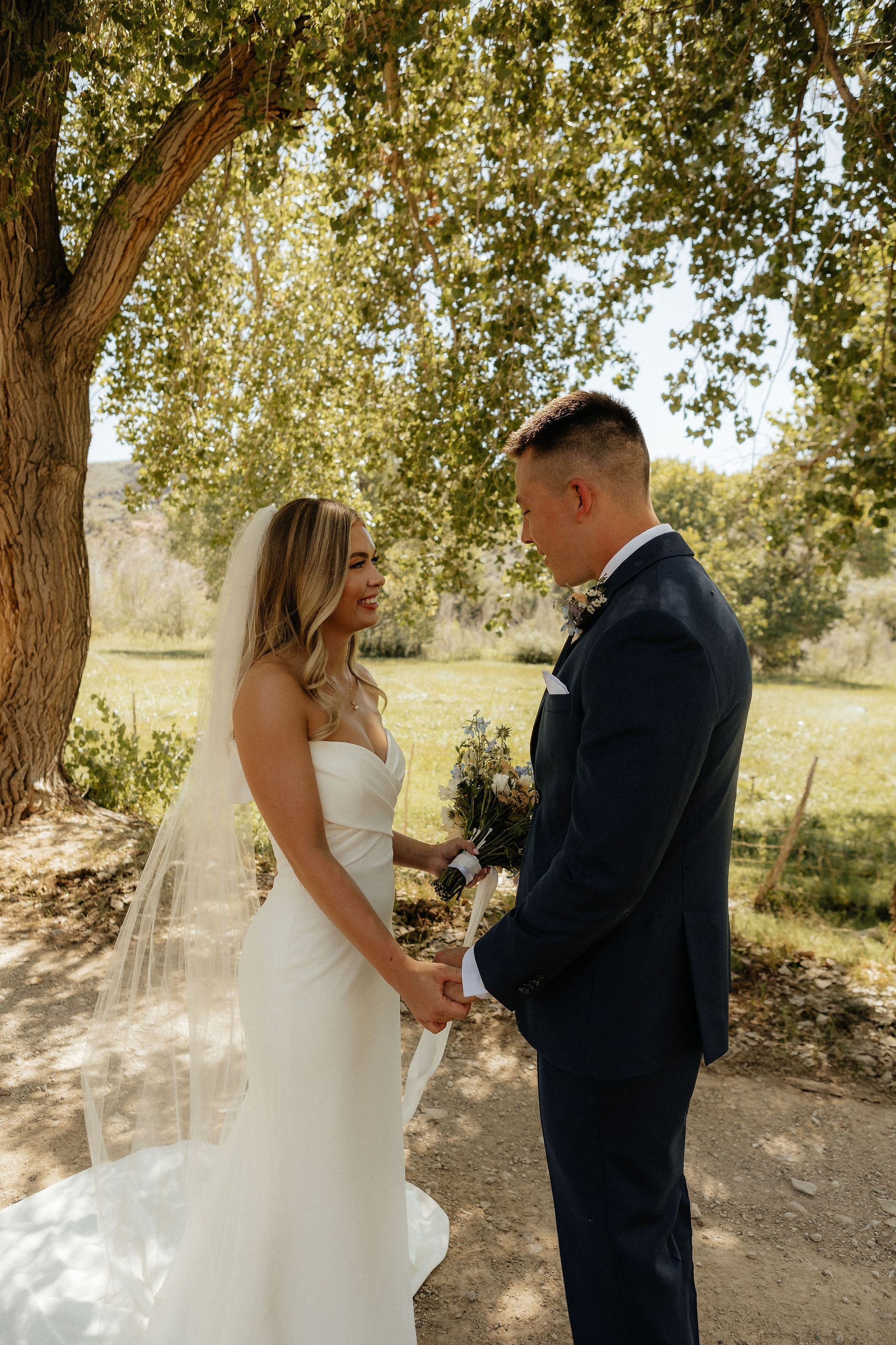 Bride and groom holding hands outdoors under a tree during their wedding ceremony