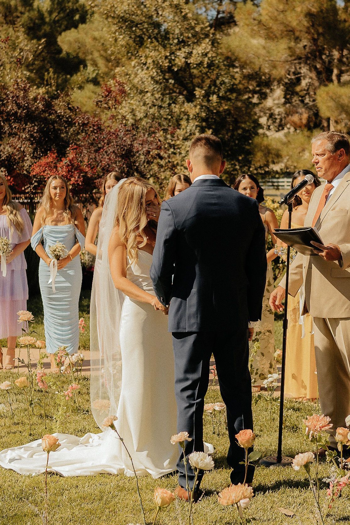 Outdoor wedding ceremony with bride and groom facing an officiant under trees