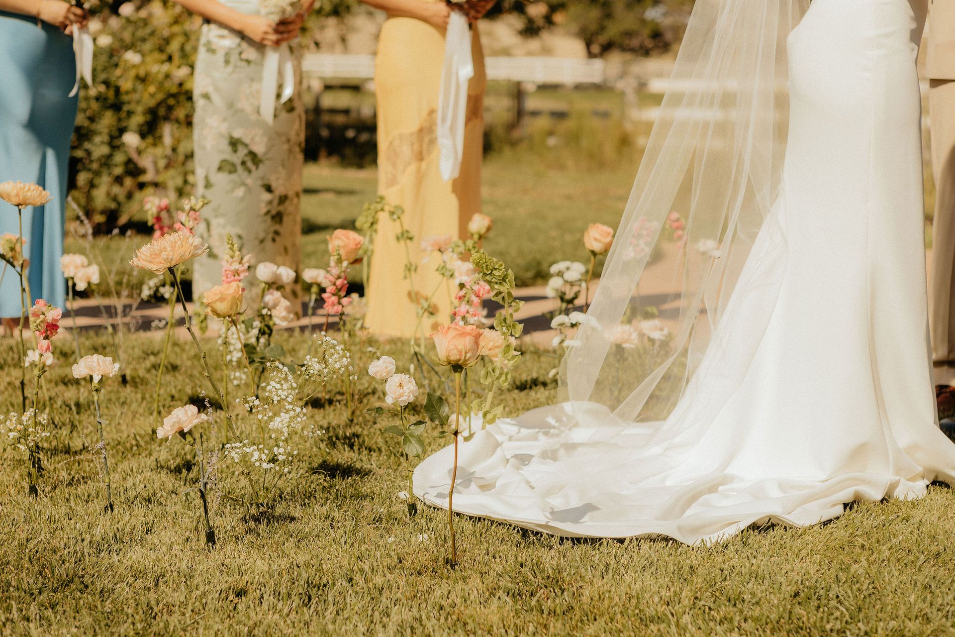 Bride’s white dress and veil on a garden lawn with pastel flowers and hanging decorations