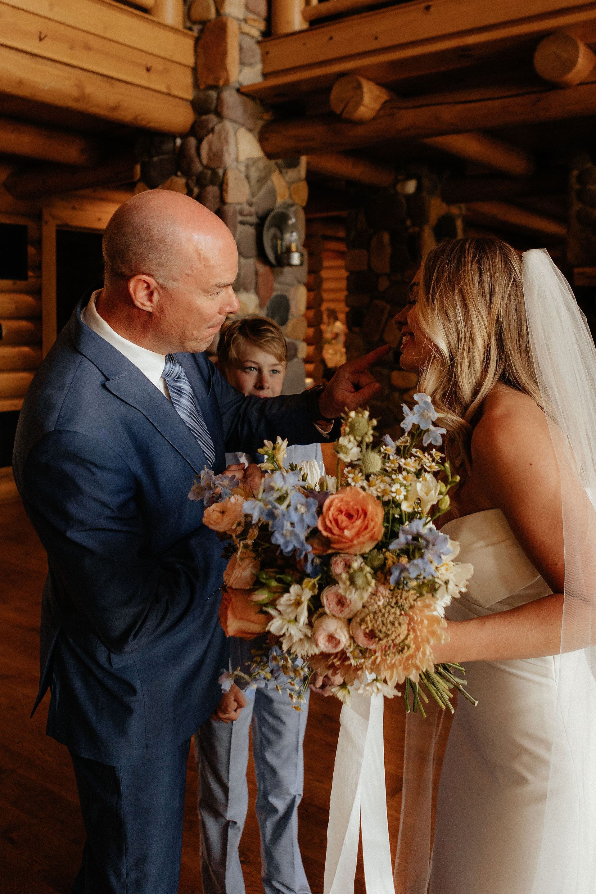 Bride and groom exchanging vows in a rustic log cabin, holding a colorful bouquet
