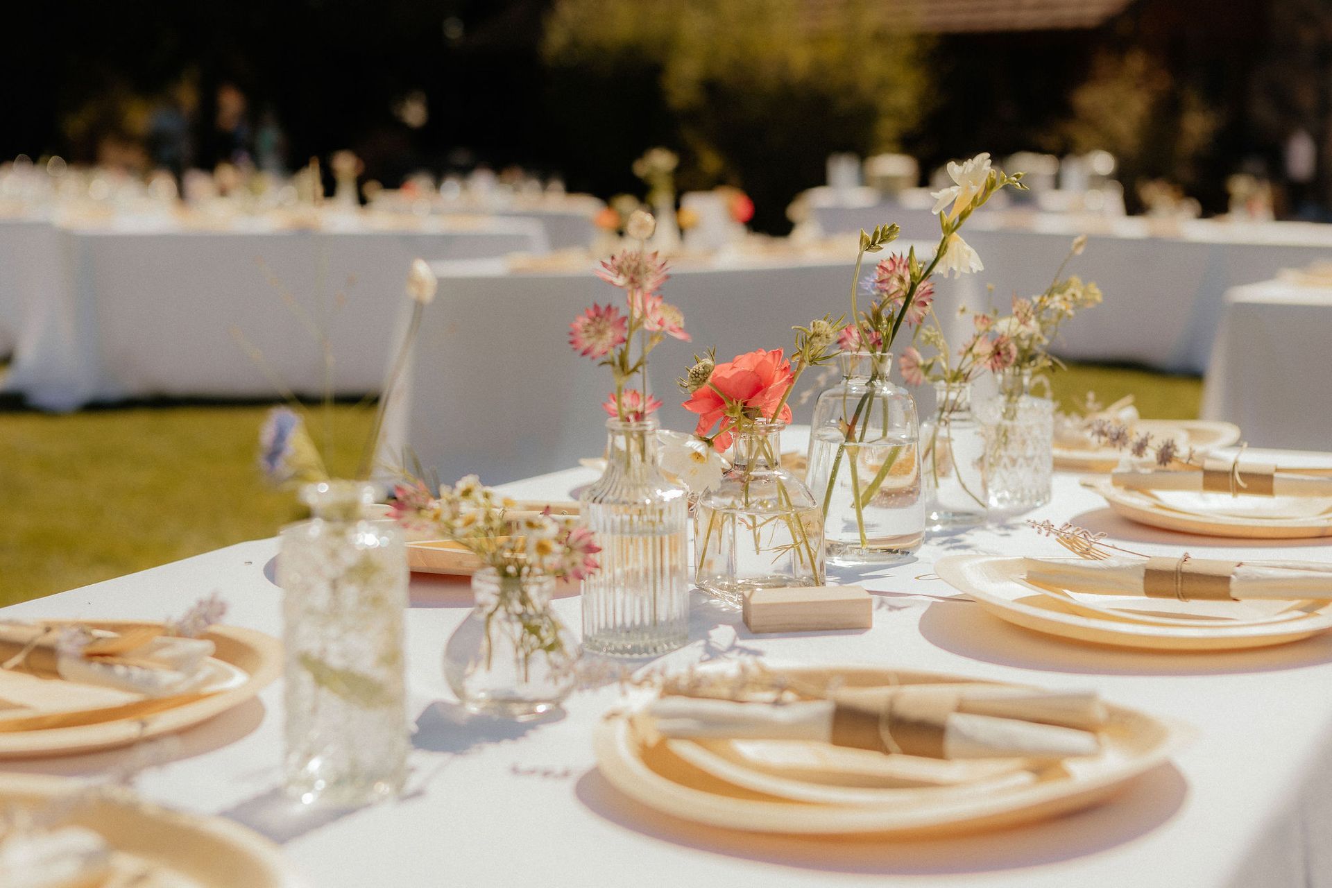 Elegant outdoor dining table set with white linens, gold plates, glassware, and pink floral centerpieces