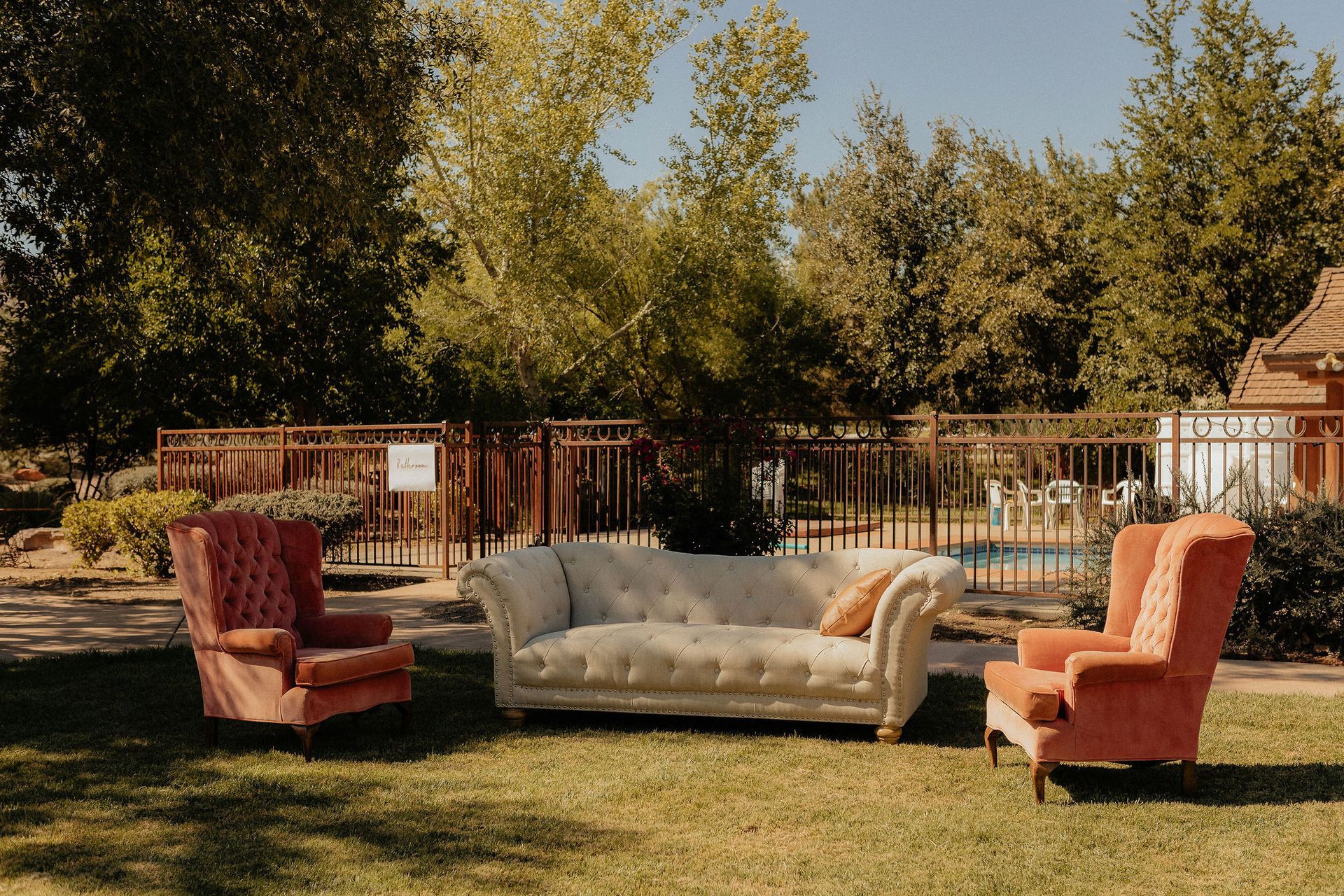 Outdoor seating area with red armchairs and a beige sofa on grass under trees