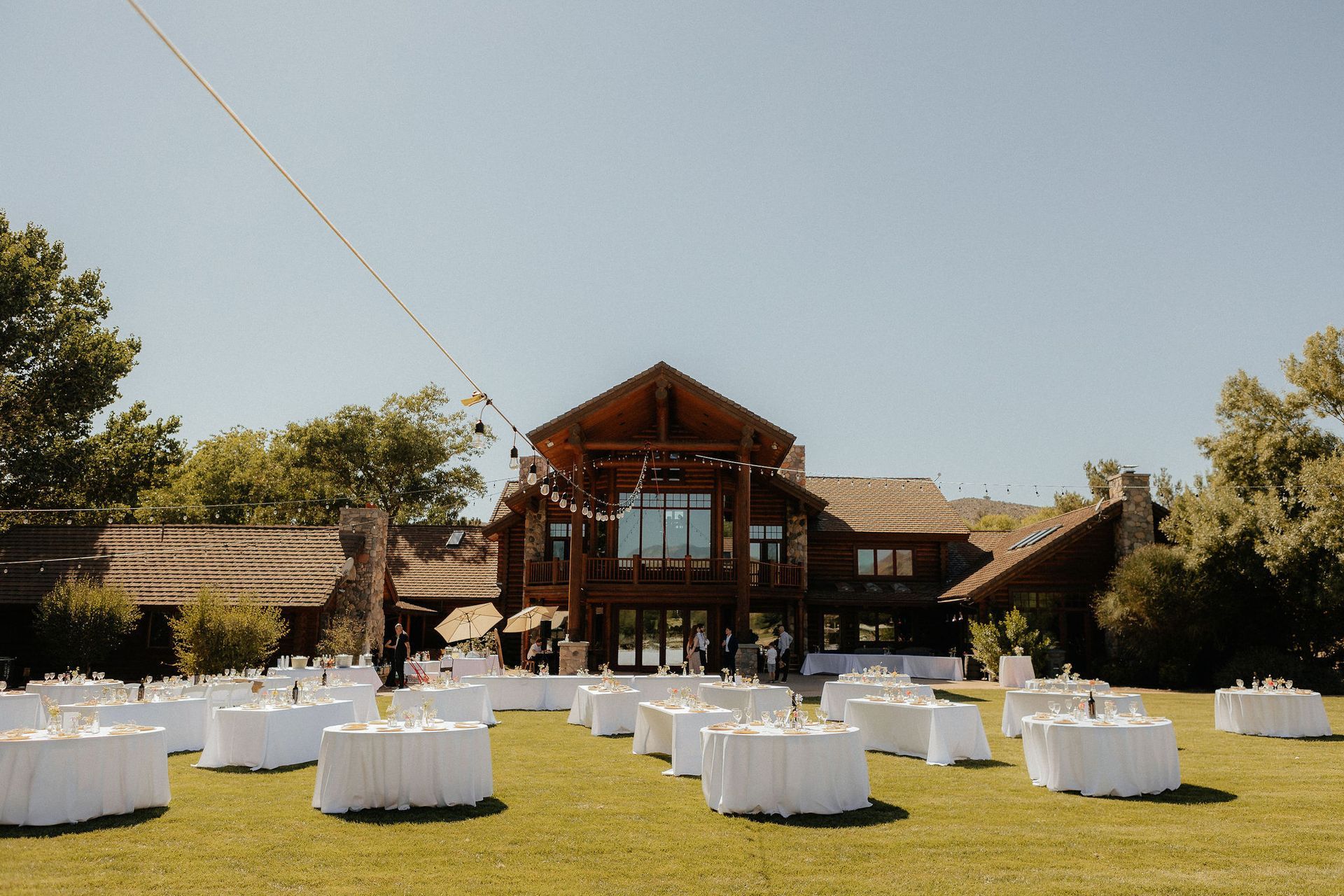 Outdoor event setup on a lawn with white-covered tables in front of a chalet-style building
