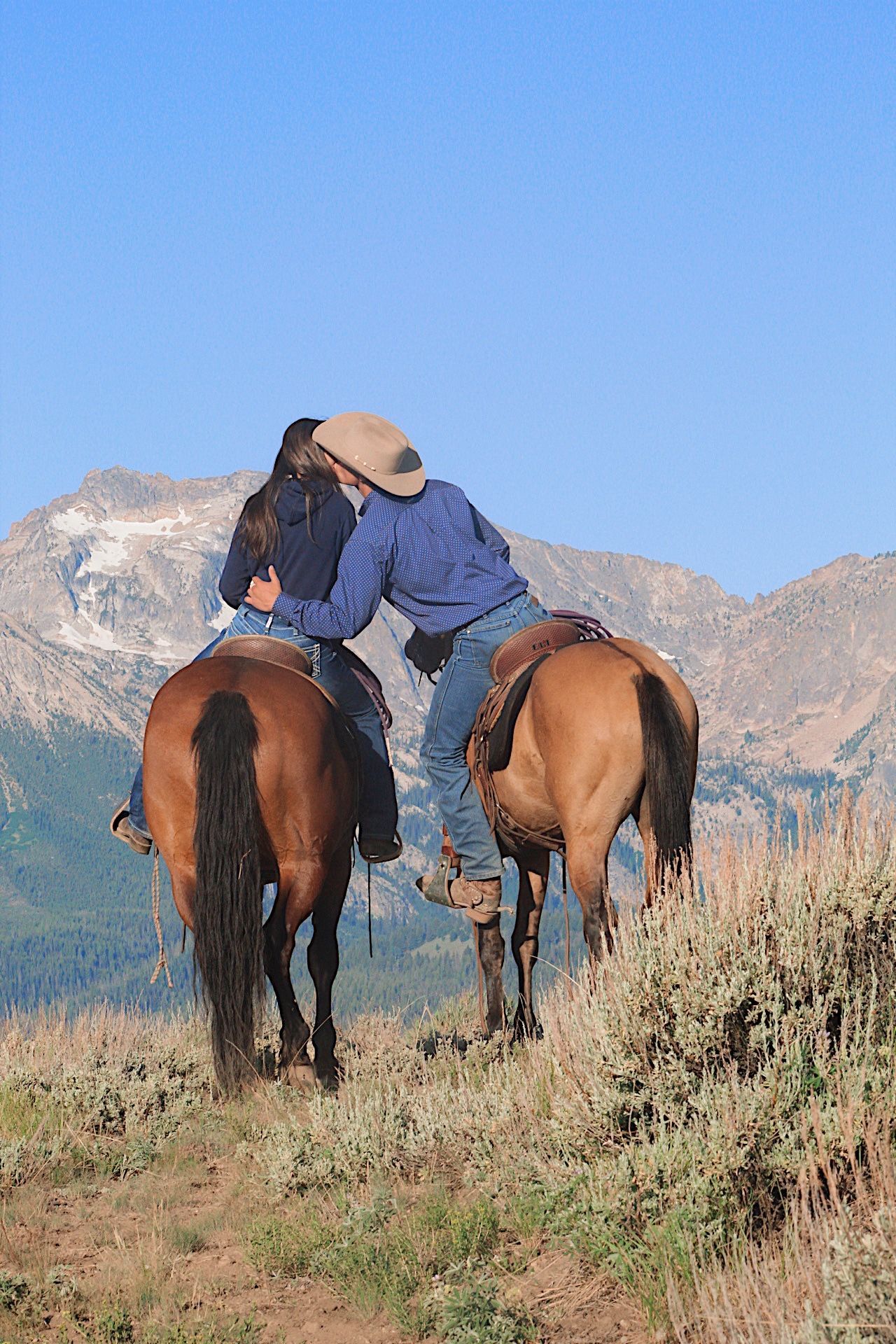 Two riders on horseback in a mountain meadow under a clear blue sky