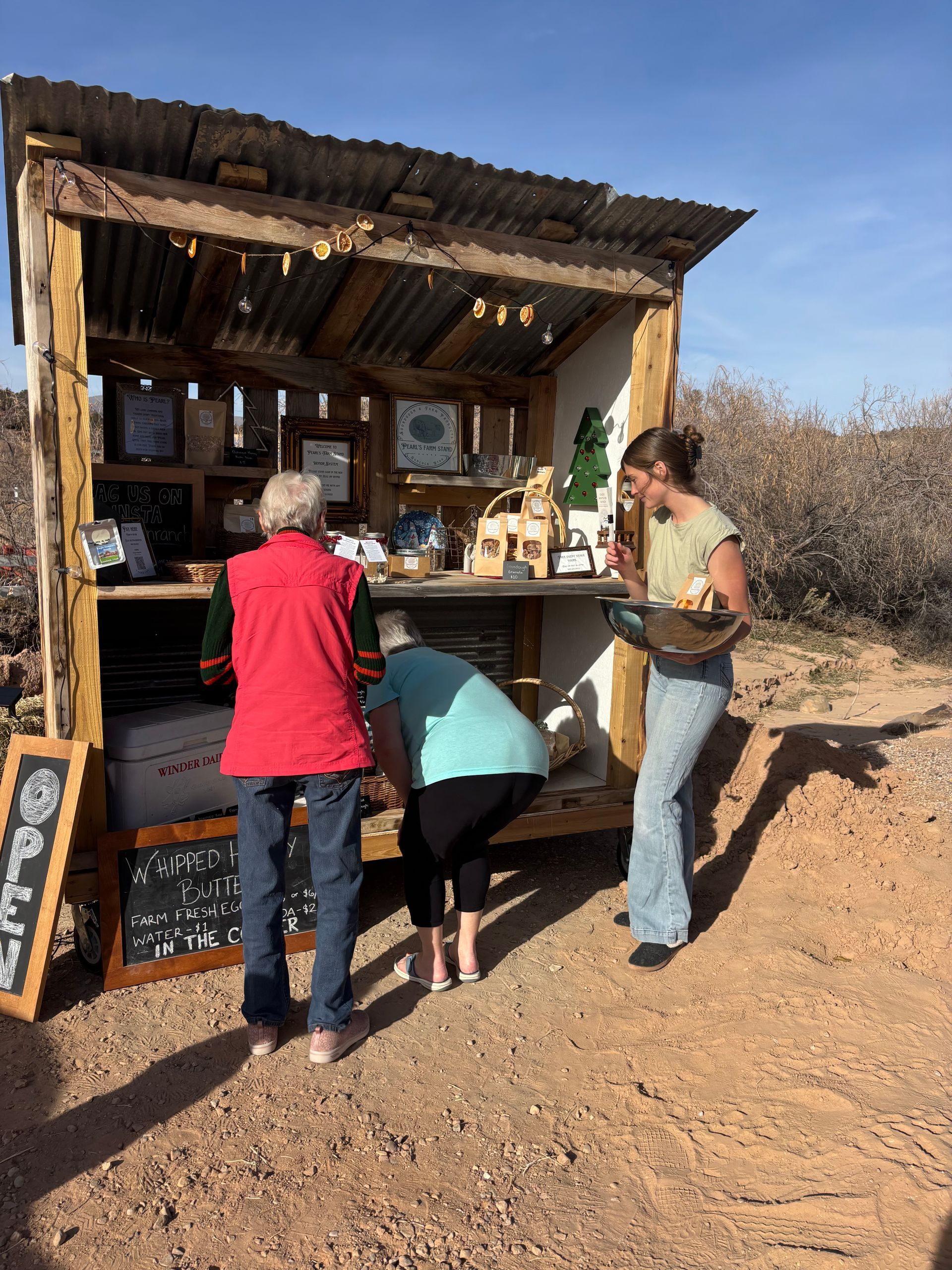 People serving drinks at a rustic outdoor stand in a dry, sunny landscape