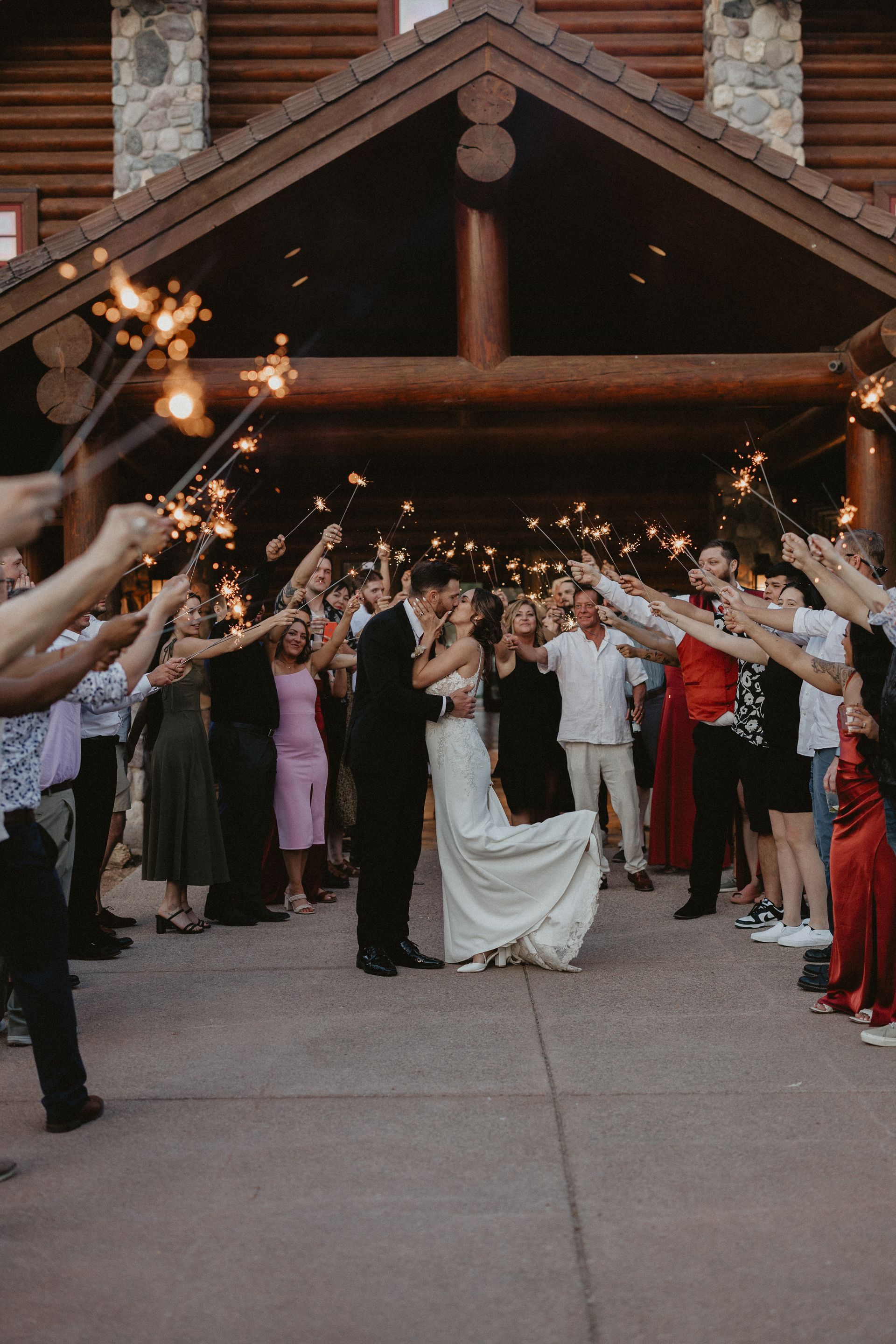 Newlyweds walking through a sparkler send-off outside a rustic venue at dusk
