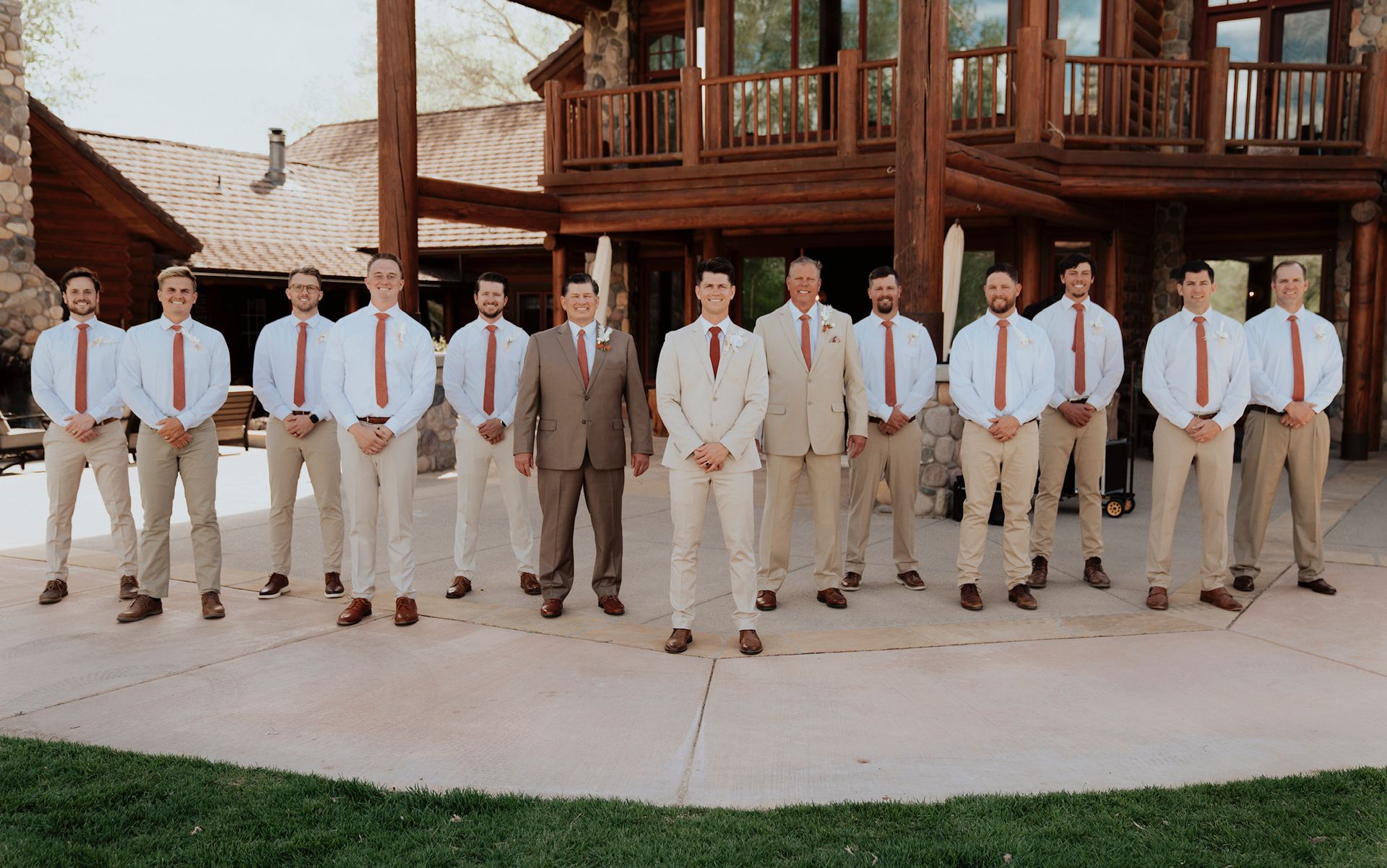 A group of people in formal attire standing outdoors in front of a wooden building and staircase.