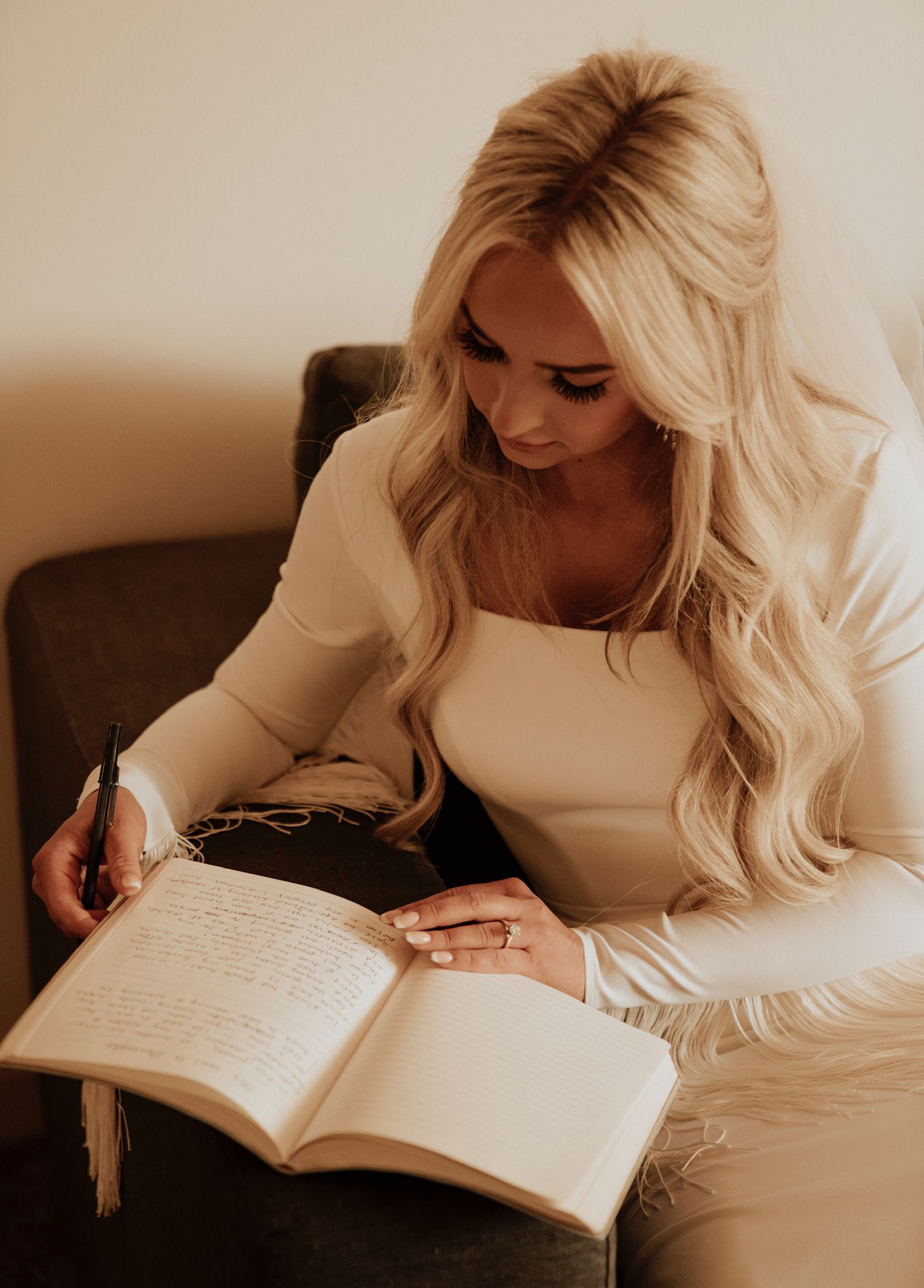 Woman writing in an open notebook on a couch, with long blonde hair and a cream sweater.