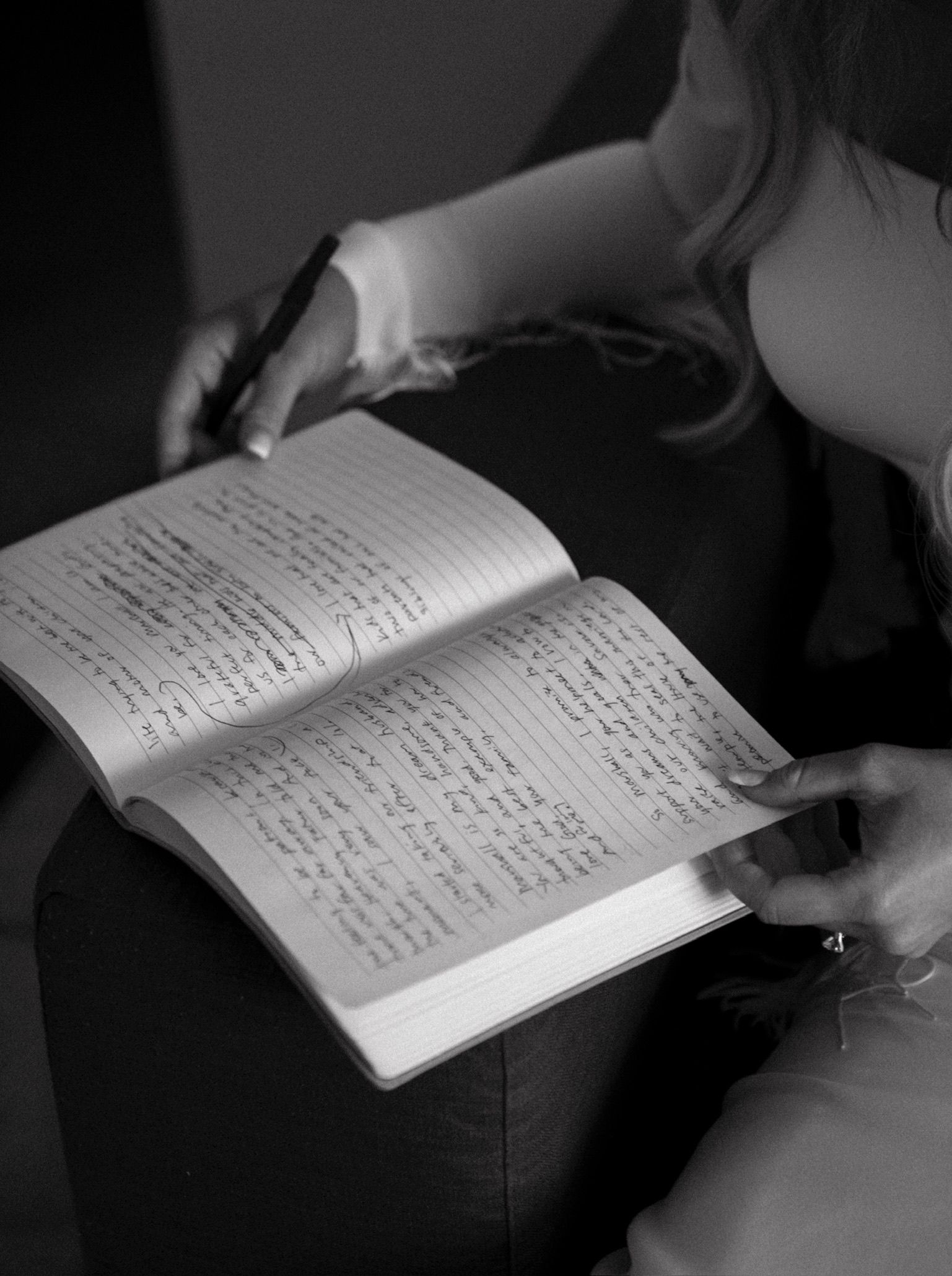 Person writing in an open notebook on a couch, with another hand holding the page.