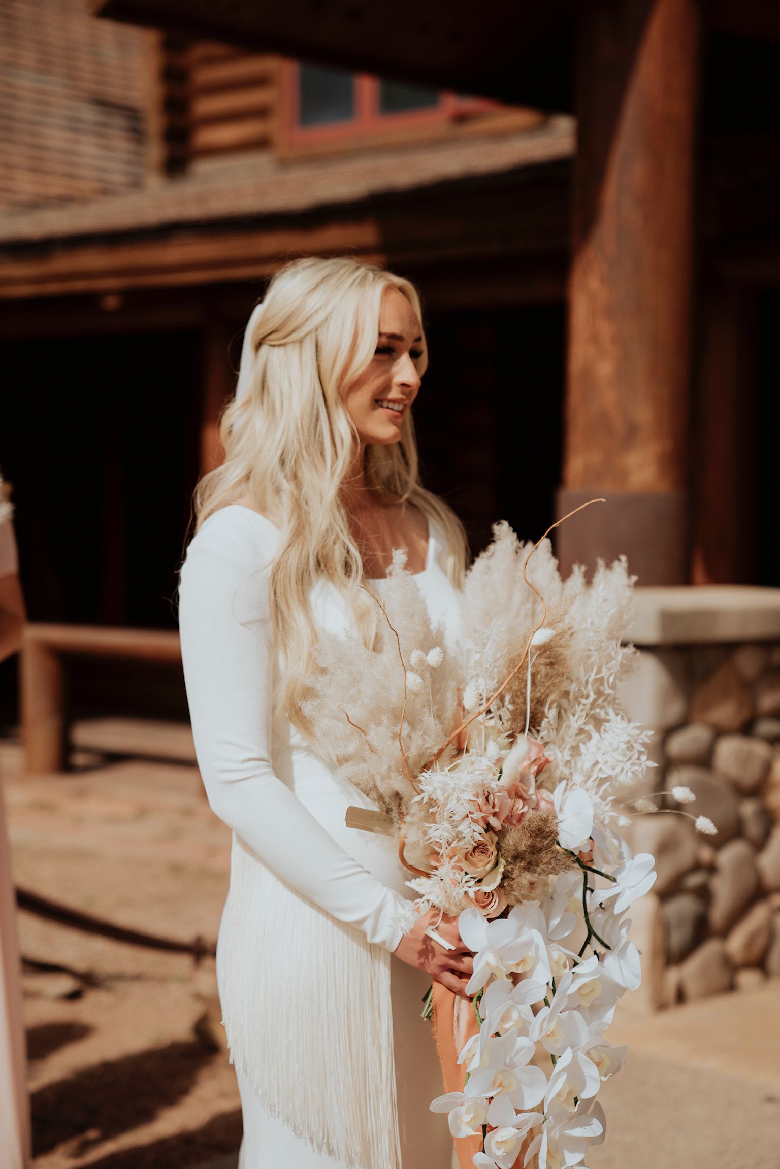 Woman in a white dress holding a bouquet at an outdoor rustic venue