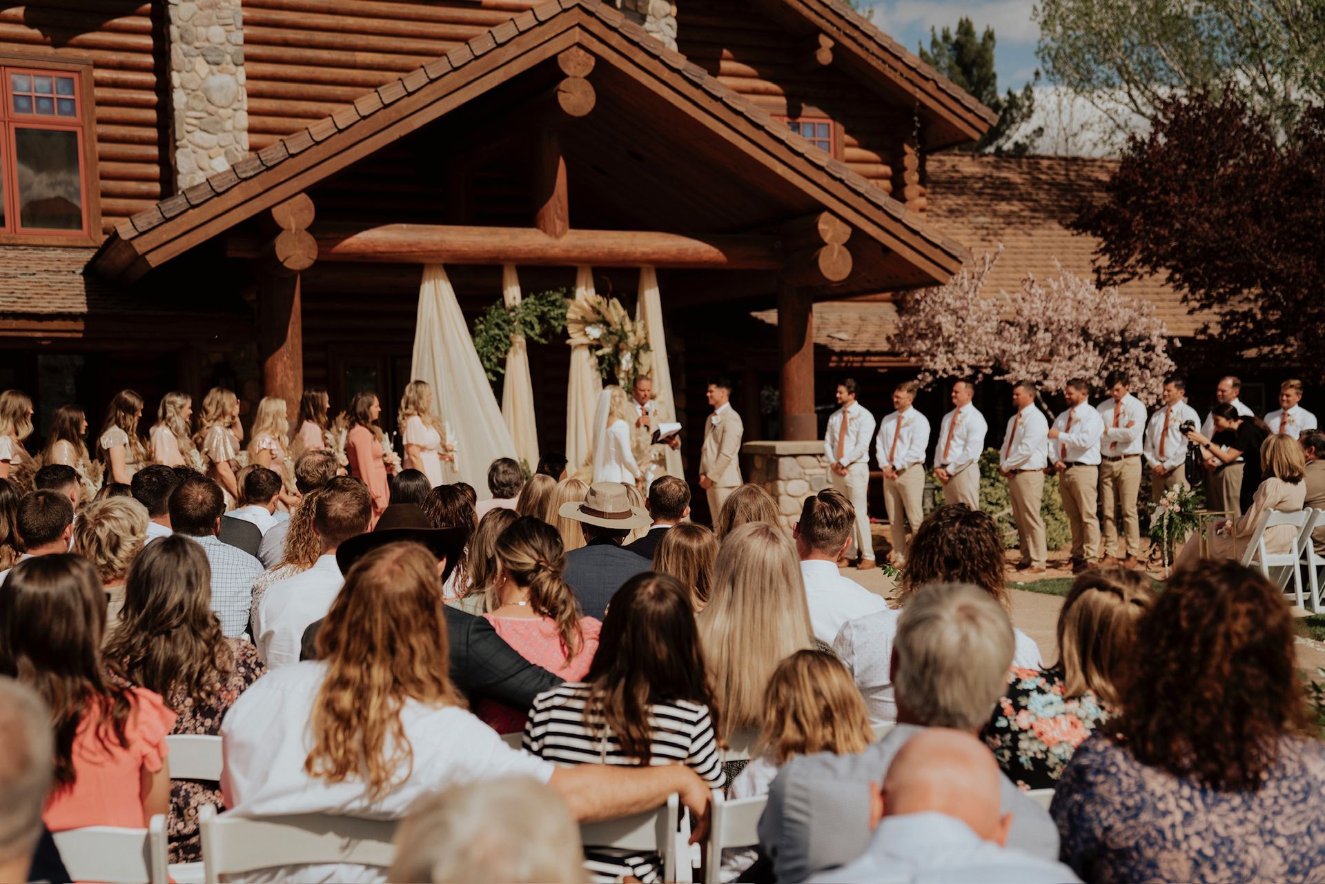 Outdoor wedding ceremony at a rustic lodge with guests seated in front of the altar and bridal party standing nearby