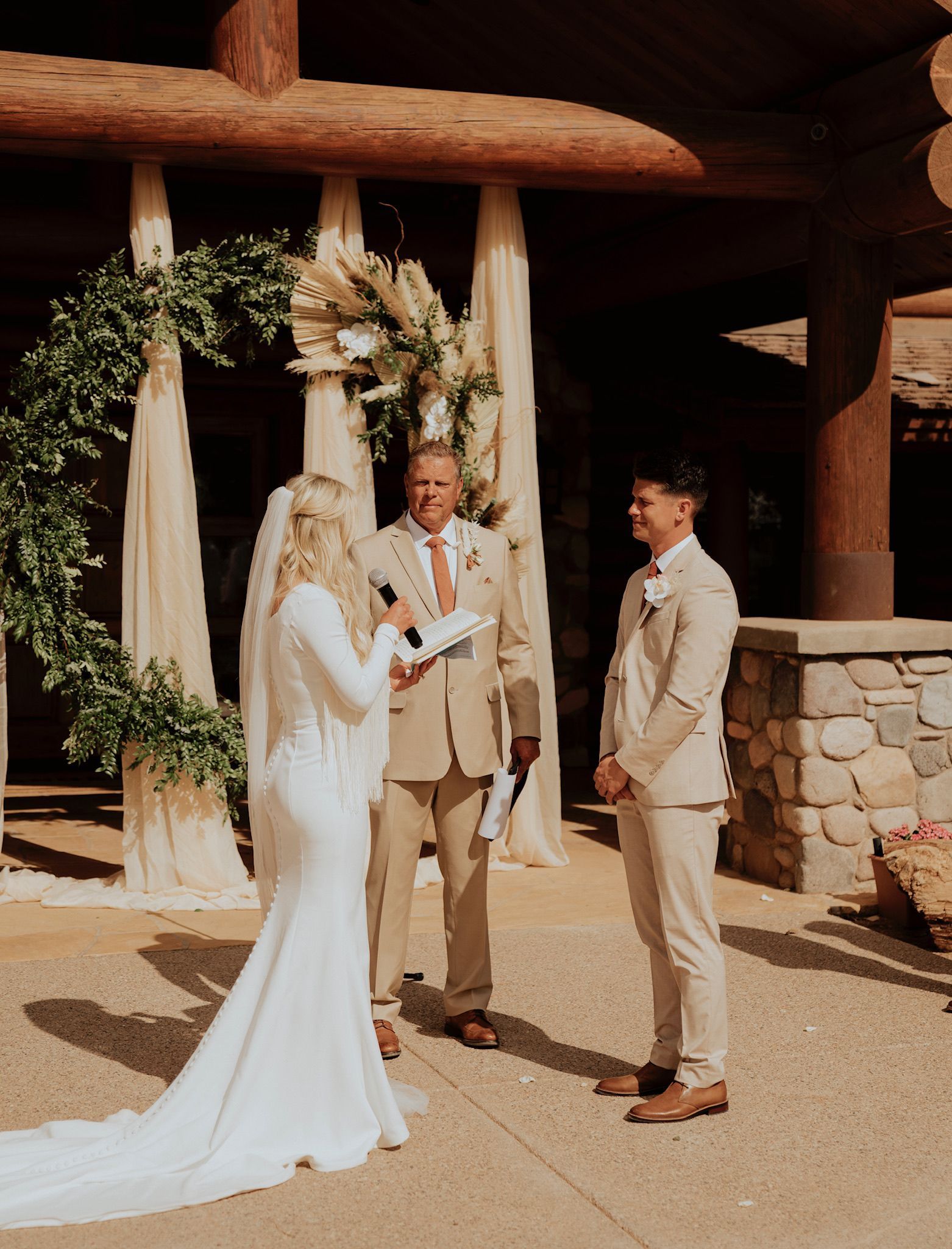 Bride and two groomsmen at an outdoor wedding ceremony under a floral arch