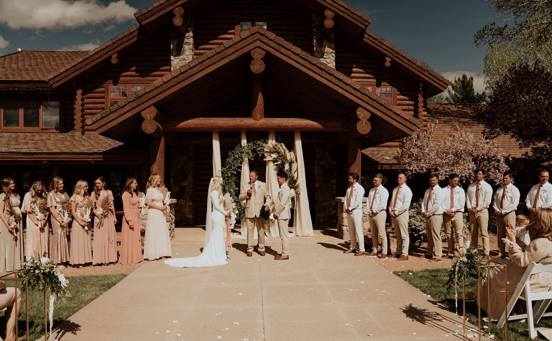 Wedding party lined up outside a rustic wooden lodge, with bride and groom centered at the entrance.