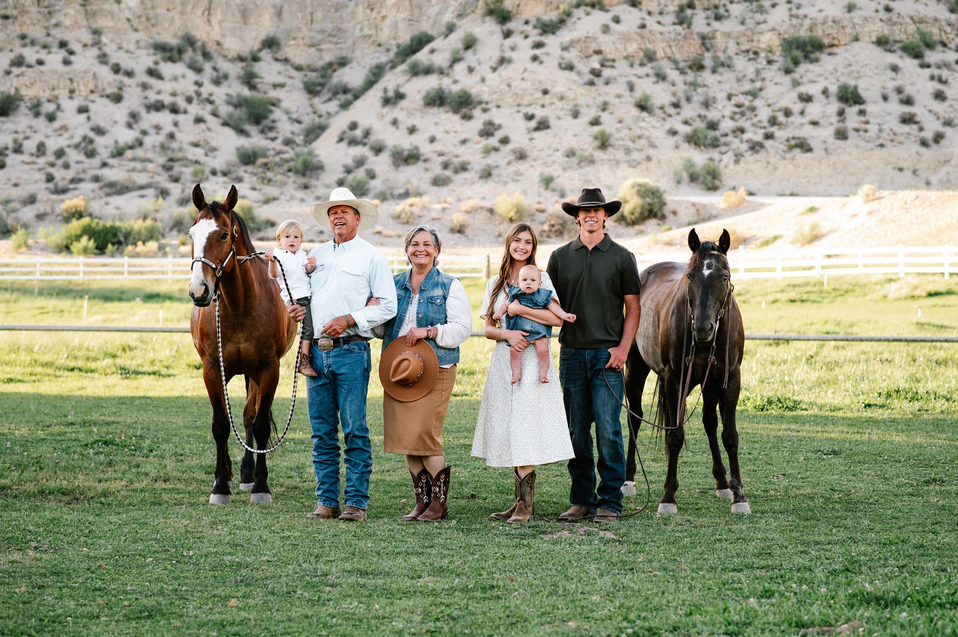 Five people and two horses standing on grass with mountains in the background