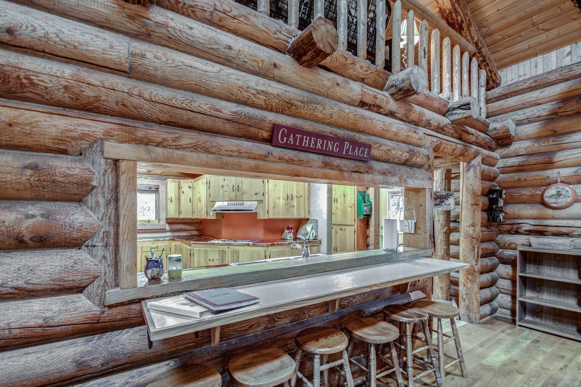 Rustic log cabin bar with wooden counter, stools, and service window to a kitchen
