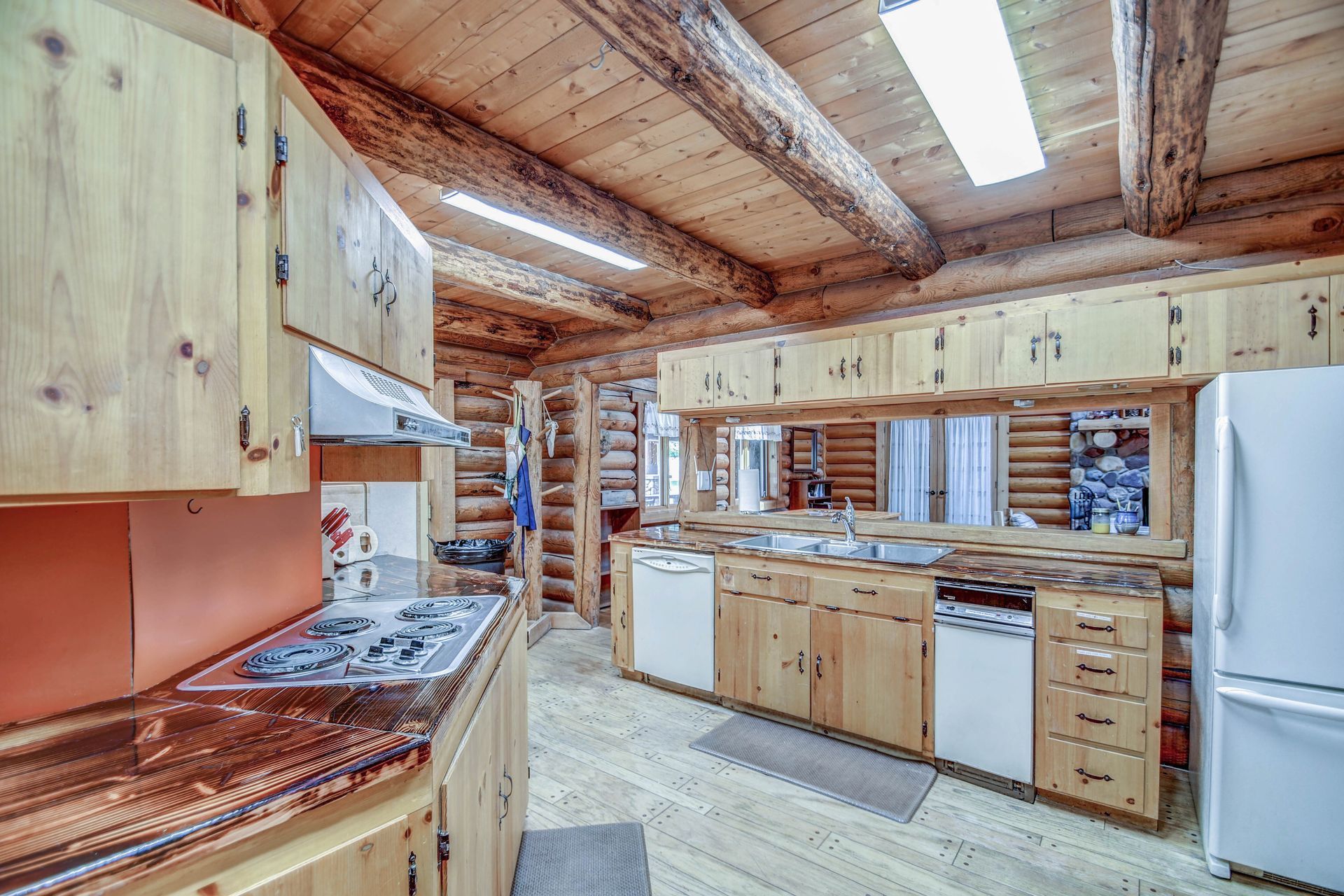 Rustic log cabin kitchen with wood cabinets, white appliances, and skylights illuminating the room