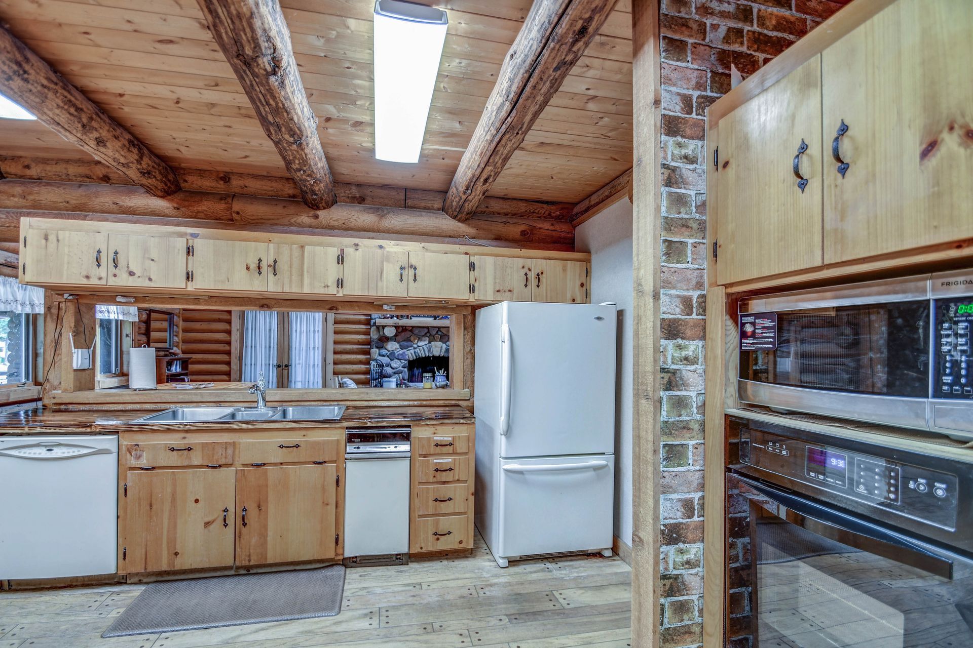 Rustic kitchen with wood cabinets, white appliances, exposed brick, and a long fluorescent ceiling light